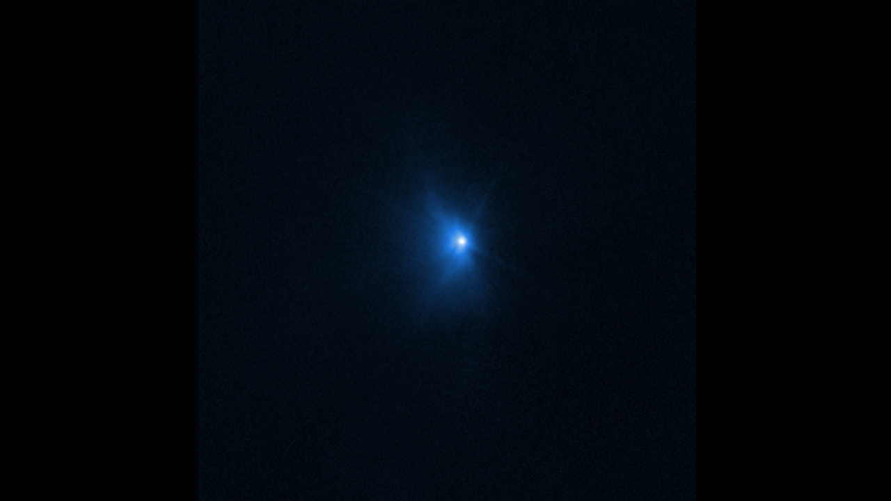 On a black background, a bright blue spot is at center. A smoke-like feature starts emitting from the blue spot on the left side, as the asteroid is impacted by the spacecraft.