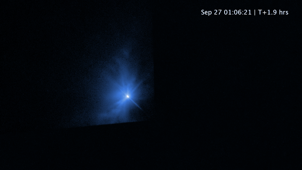 Image labeled “September 27; 01:06:21; T+1.9 hours” showing a bright white spot by an irregular cloud of blue. The background is black and there are subtle diffraction spikes radiating from the bright spot.