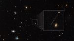 A Hubble image of a black, deep-space field is speckled with galaxies and one, lone star. In the center of the image is a small, white-bordered, boxed area that contains one, long, thin, diagonal streak of whitish-blue stars and two galaxies. To the right of the small box is a larger, white-bordered box that contains a magnified view of the contents of smaller box.