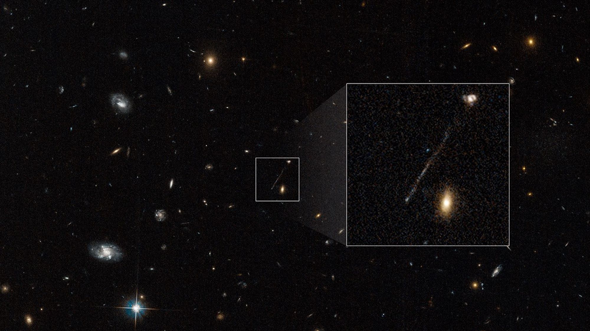 A Hubble image of a black, deep-space field is speckled with galaxies and one, lone star. In the center of the image is a small, white-bordered, boxed area that contains one, long, thin, diagonal streak of whitish-blue stars and two galaxies. To the right of the small box is a larger, white-bordered box that contains a magnified view of the contents of smaller box.