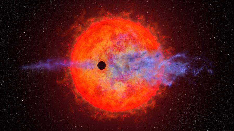This illustration shows the ball of a red dwarf star. It is mottled with dark spots and finger-like filamentary outbursts. In front is a much smaller black circle representing the silhouette of a planet passing in front of the star. The red dwarf's furious activity is causing the planet's atmosphere to escape into space. This appears as wispy blue filaments along the planet's straight horizontal orbital path. The star is colored a rich red because it is cooler than our Sun.