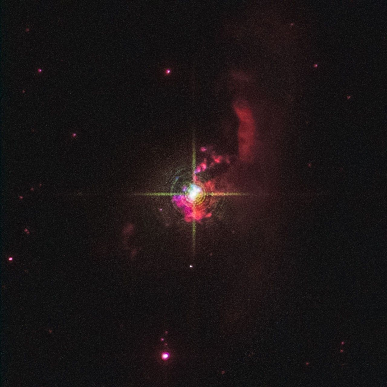 At the center of the image is a bright white star with four prominent diffraction spikes. The star is surrounded by red clumps. A more translucent, red finger-shaped cloud of vertical material begins at the star's upper right, and goes a bit above it. The black background of space is sprinkled with tiny red and white stars.