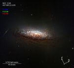 A compass and scale image titled NGC 1546 HST WFC3/UVIS, against the black background of space. Near top left is a color key with filters: blue (F438W), green (F555W), red (F814W). At center is a Hubble image of the nearby galaxy NGC 1546. The galaxy's orientation gives us a good view of dust lanes from slightly above and backlit by the galaxy's core. This dust absorbs light from the core, reddening it and making the dust appear rusty-brown. The core itself glows brightly in a yellowish light indicating an older population of stars. Brilliant-blue regions of active star formation sparkle through the dust. Several background galaxies also are visible, including an edge-on spiral just to the left of NGC 1546. At bottom right are white compass arrows. The arrow pointing to the 10 o'clock position is labeled E for east; the arrow pointing to the 2 o'clock position is labeled N for north. At bottom left is a scale bar labeled 9,700 light-years over 40 arc seconds.