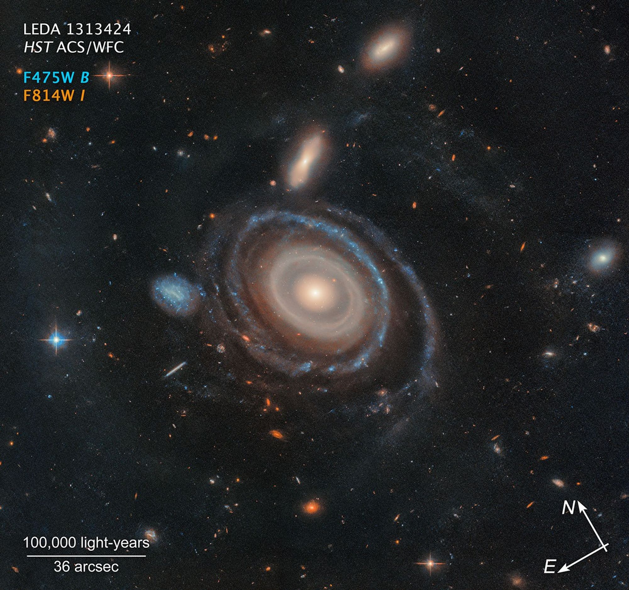 A graphic labeled “LEDA 1313424, HST ACS/WFC.” At the center is a large galaxy with a significantly smaller galaxy to its center-left on the black background of space.