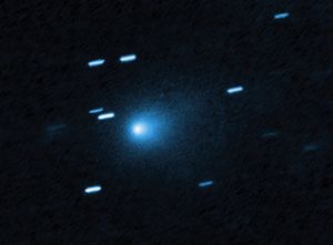 At the center of the image is a comet that appears as a teardrop-shaped bluish cocoon of dust coming off the comet’s solid, icy nucleus and seen against a black background. The comet appears to be heading to the bottom left corner of the image. About a dozen short, light blue diagonal streaks are seen scattered across the image, which are from background stars that appeared to move during the exposure because the telescope was tracking the moving comet.