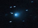 At the center of the image is a comet that appears as a teardrop-shaped bluish cocoon of dust coming off the comet's solid, icy nucleus and seen against a black background. The comet appears to be heading to the bottom left corner of the image. About a dozen short, light blue diagonal streaks are seen scattered across the image, which are from background stars that appeared to move during the exposure because the telescope was tracking the moving comet.