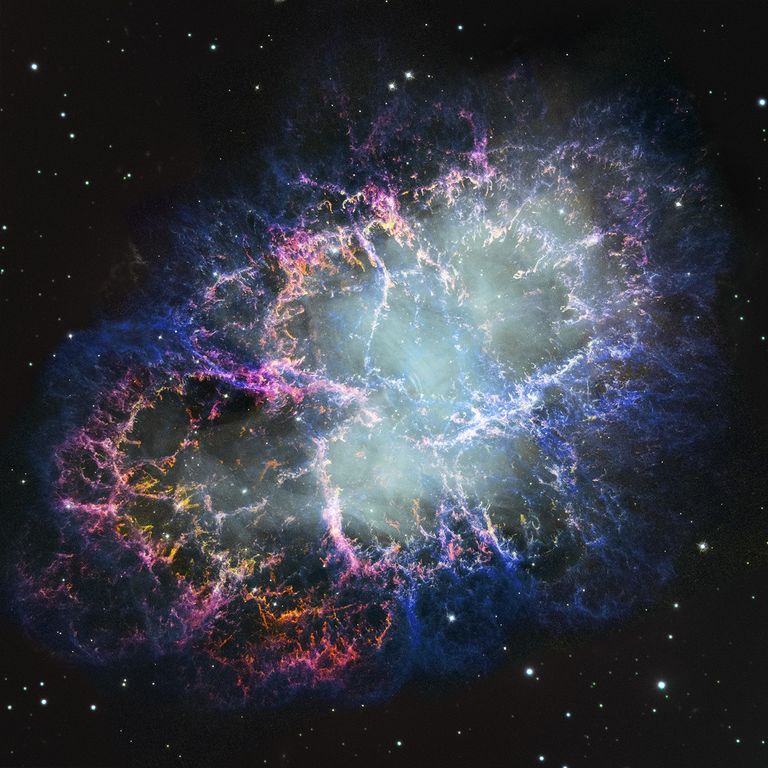 A colorful nebula of thick filaments of cosmic dust and gas appears to splash outward from a hazy white center. Colors include bright pink, blue, and orange. Small white stars dot the background.