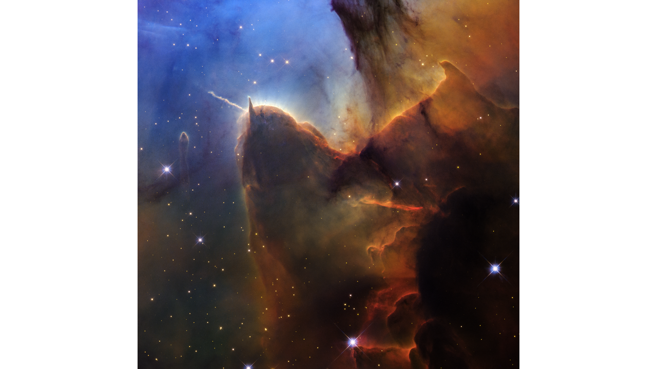A tightly cropped Hubble view of a vast star-forming region known as the Trifid Nebula. The top left is bright blue. Brown and amber colors run from top right through the center in irregular, overlapping lines to the bottom-center. At bottom right, the view is almost black. Tiny, amber-colored stars appear throughout.
