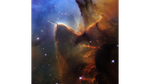 A tightly cropped Hubble view of a vast star-forming region known as the Trifid Nebula. The top left is bright blue. Brown and amber colors run from top right through the center in irregular, overlapping lines to the bottom-center. At bottom right, the view is almost black. Tiny, amber-colored stars appear throughout.