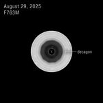 A black and white view of Saturn’s south pole, labeled “August 29, 2025” and “F763M.” The south-polar view of Saturn shows concentric bands of its atmosphere, transitioning from bright outer bands to a dark central region outlined in a 10-sided pattern. This outline is labeled “decagon.” A small, dashed circle at the very center of the pole with an “X” inside denotes missing data.