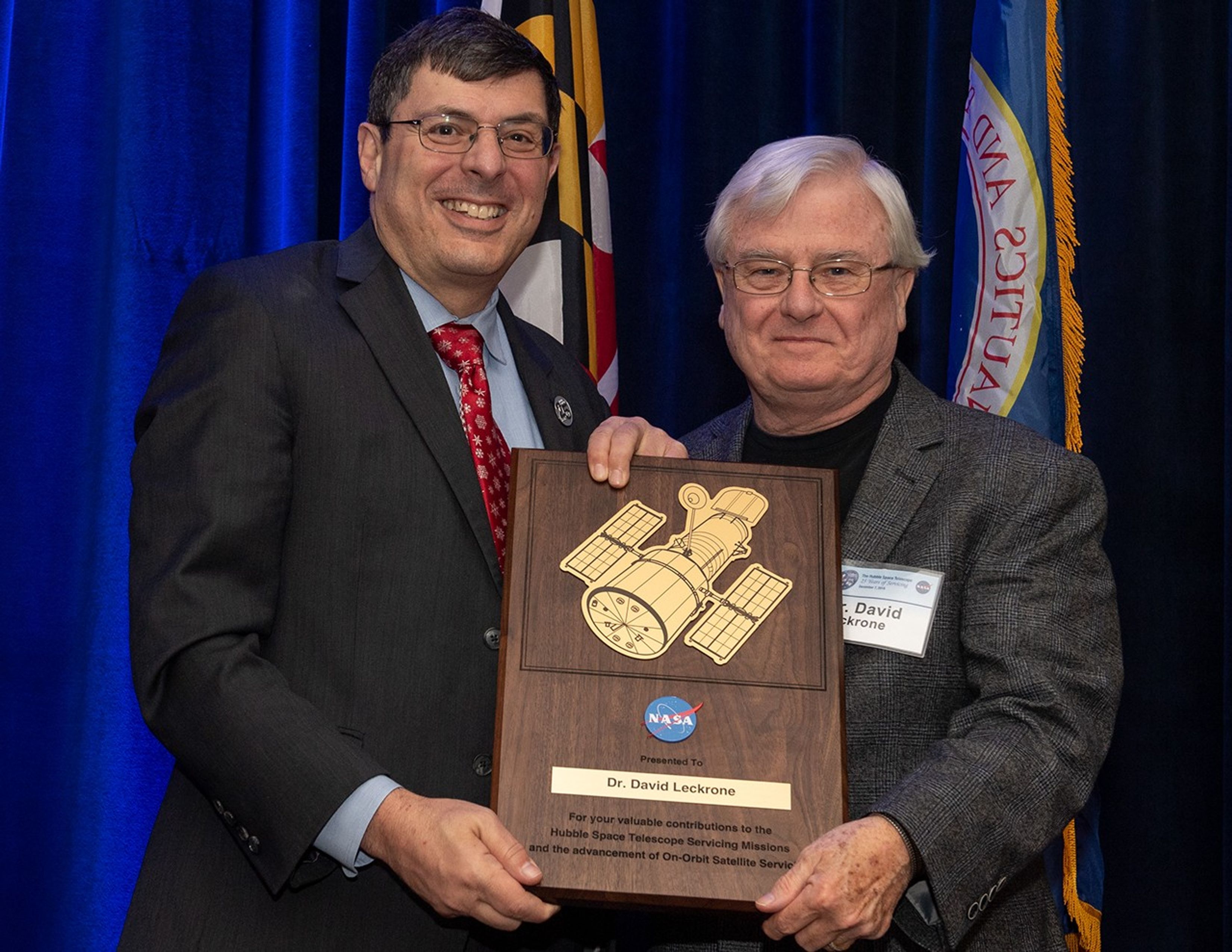 Scolese (left) and Leckrone (right) hold a wooden plaque between them with Leckrone's name and a gold graphic of Hubble on it.