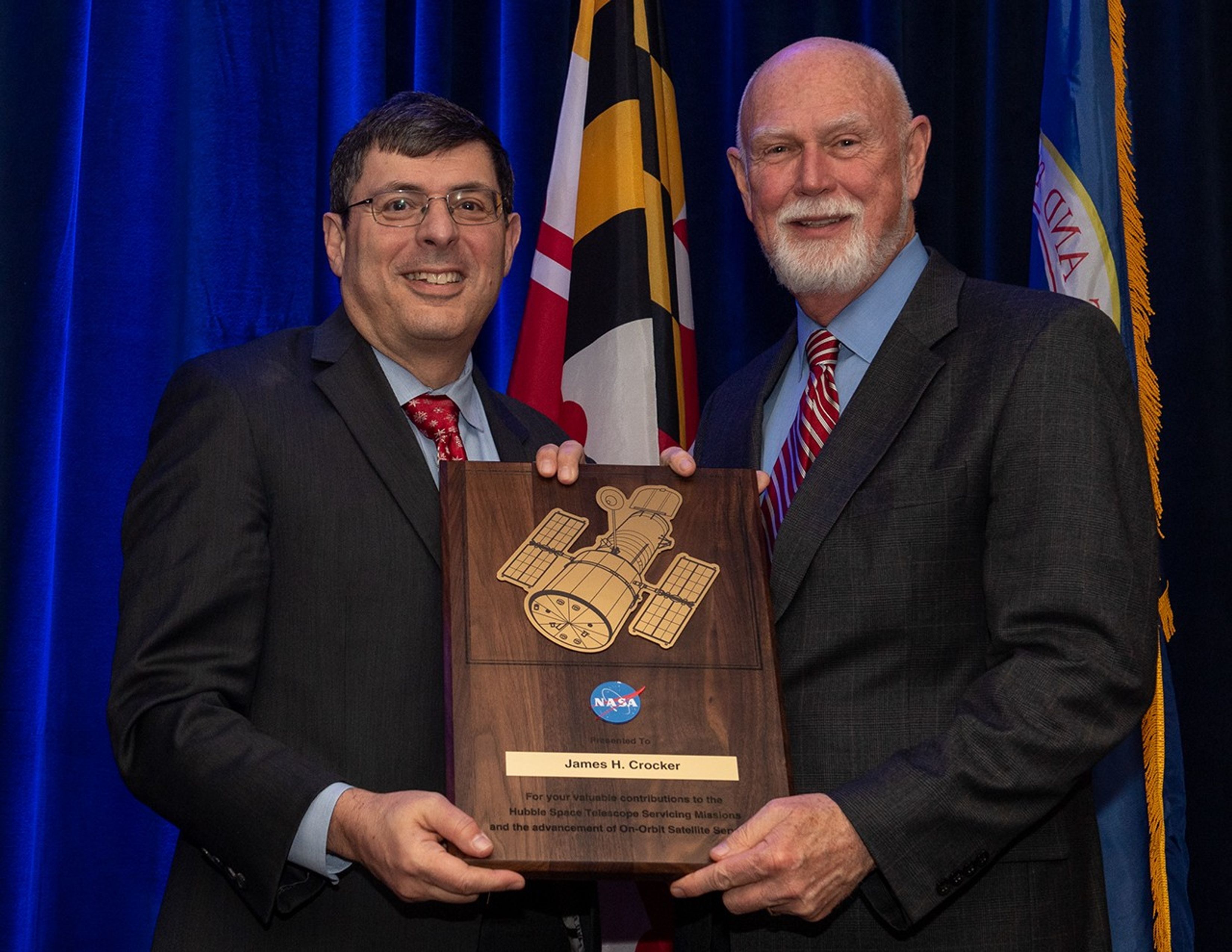 Scolese (left) and Crocker (right) hold a wooden plaque between them with Crocker's name and a gold graphic of Hubble on it.