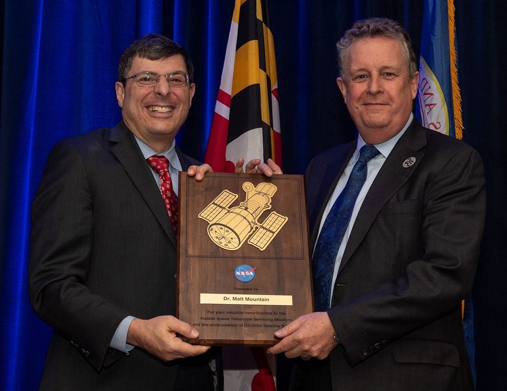 Scolese (left) and Mountain (right) hold a wooden plaque between them with Mountain's name and a gold graphic of Hubble on it.