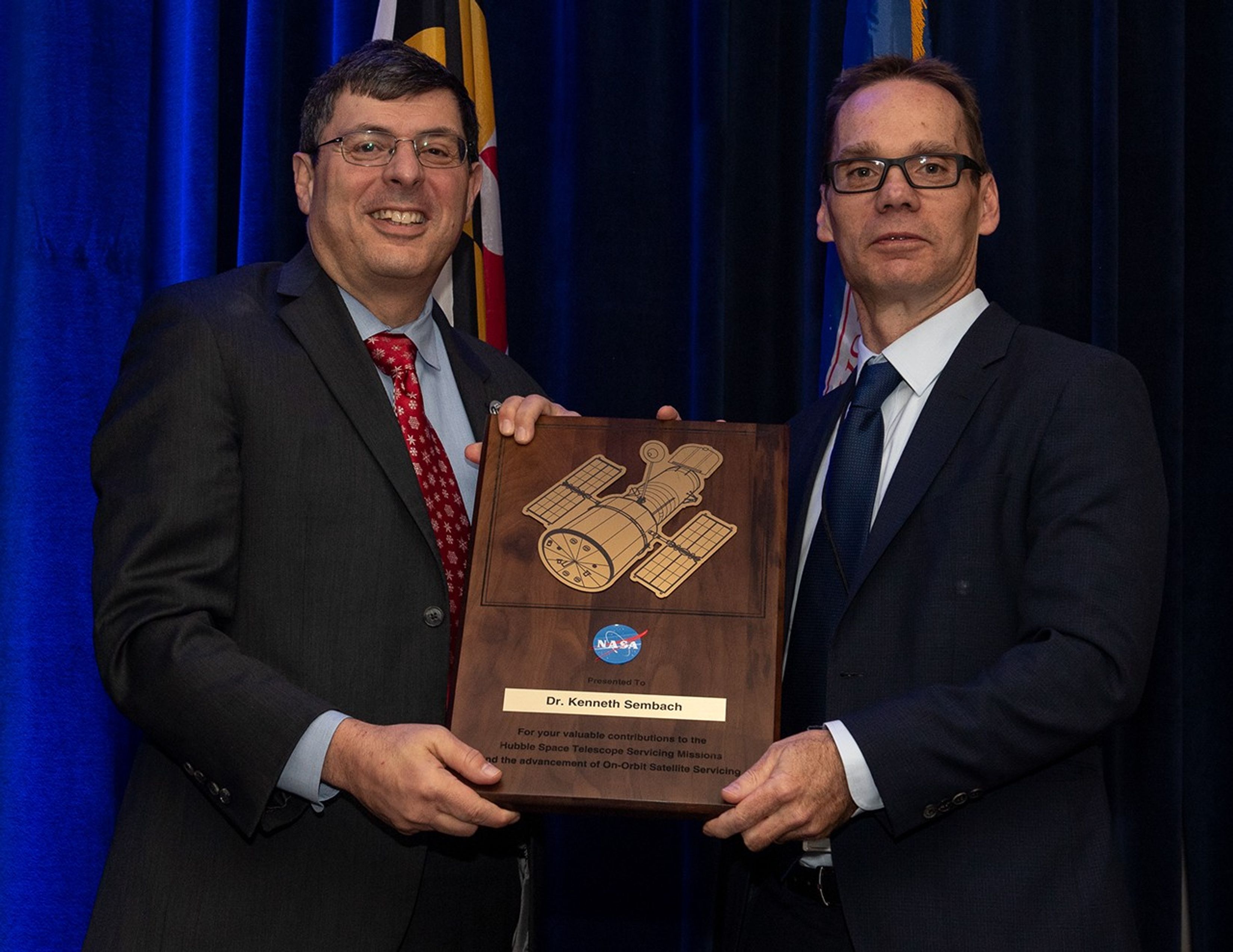 Scolese (left) and Sembach (right) hold a wooden plaque between them with Sembach's name and a gold graphic of Hubble on it.