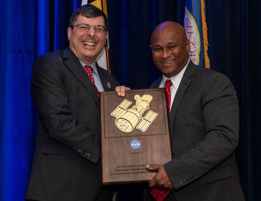 Scolese (left) and Pullen (right) hold a wooden plaque between them with a gold graphic of Hubble on it.