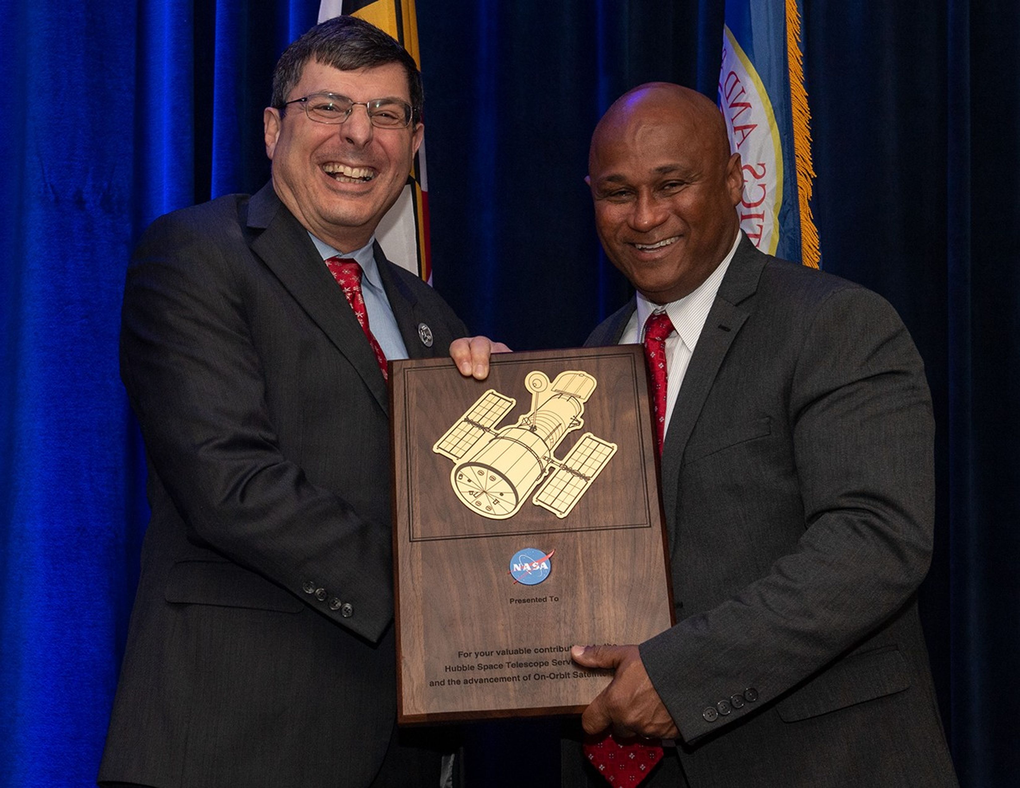 Scolese (left) and Pullen (right) hold a wooden plaque between them with a gold graphic of Hubble on it.
