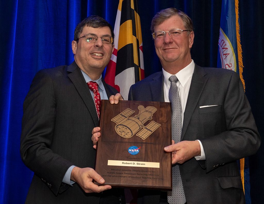 Scolese (left) and Strain (right) hold a wooden plaque between them with Strain's name and a gold graphic of Hubble on it.