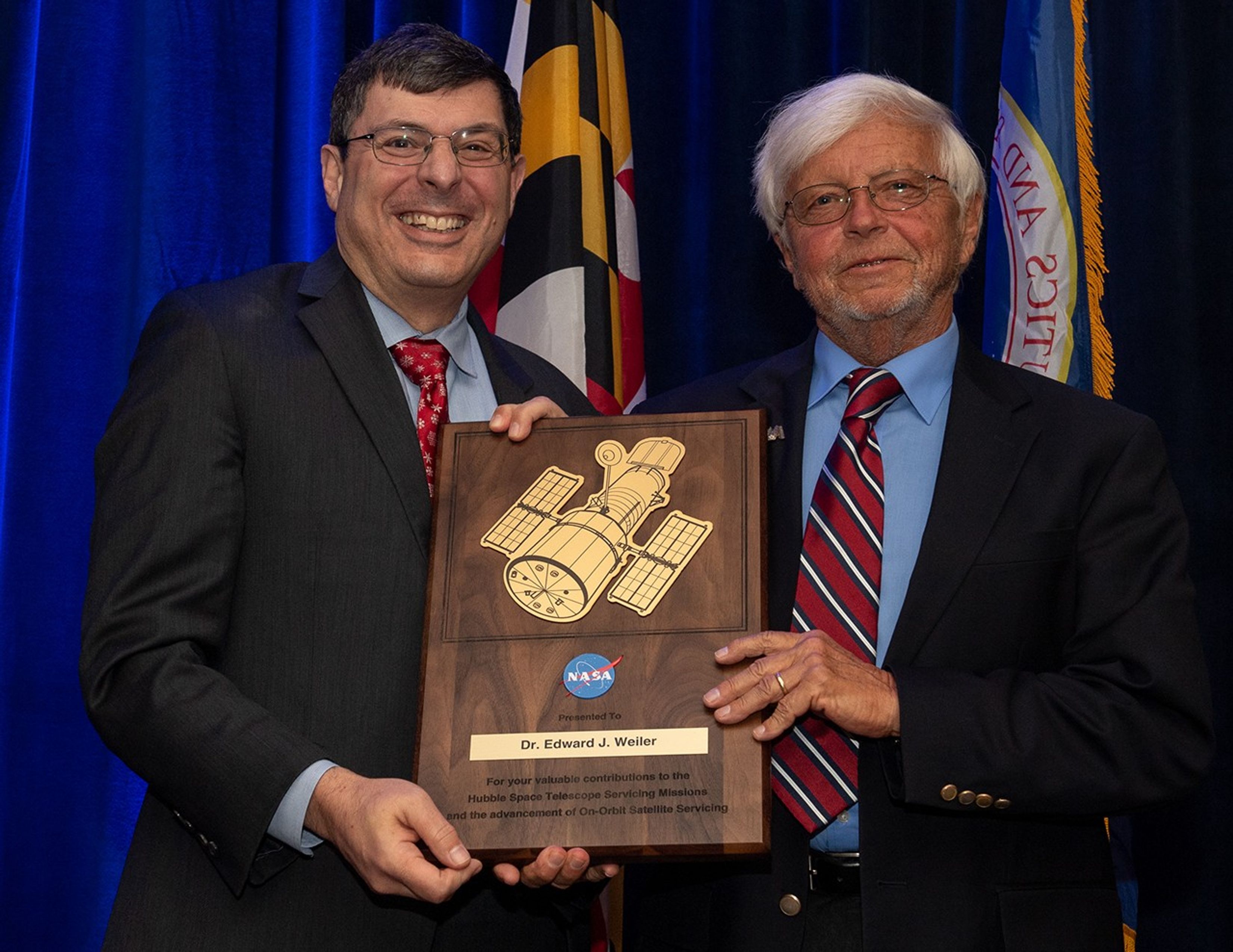 Scolese (left) and Weiler (right) hold a wooden plaque between them with Weiler's name and a gold graphic of Hubble on it.