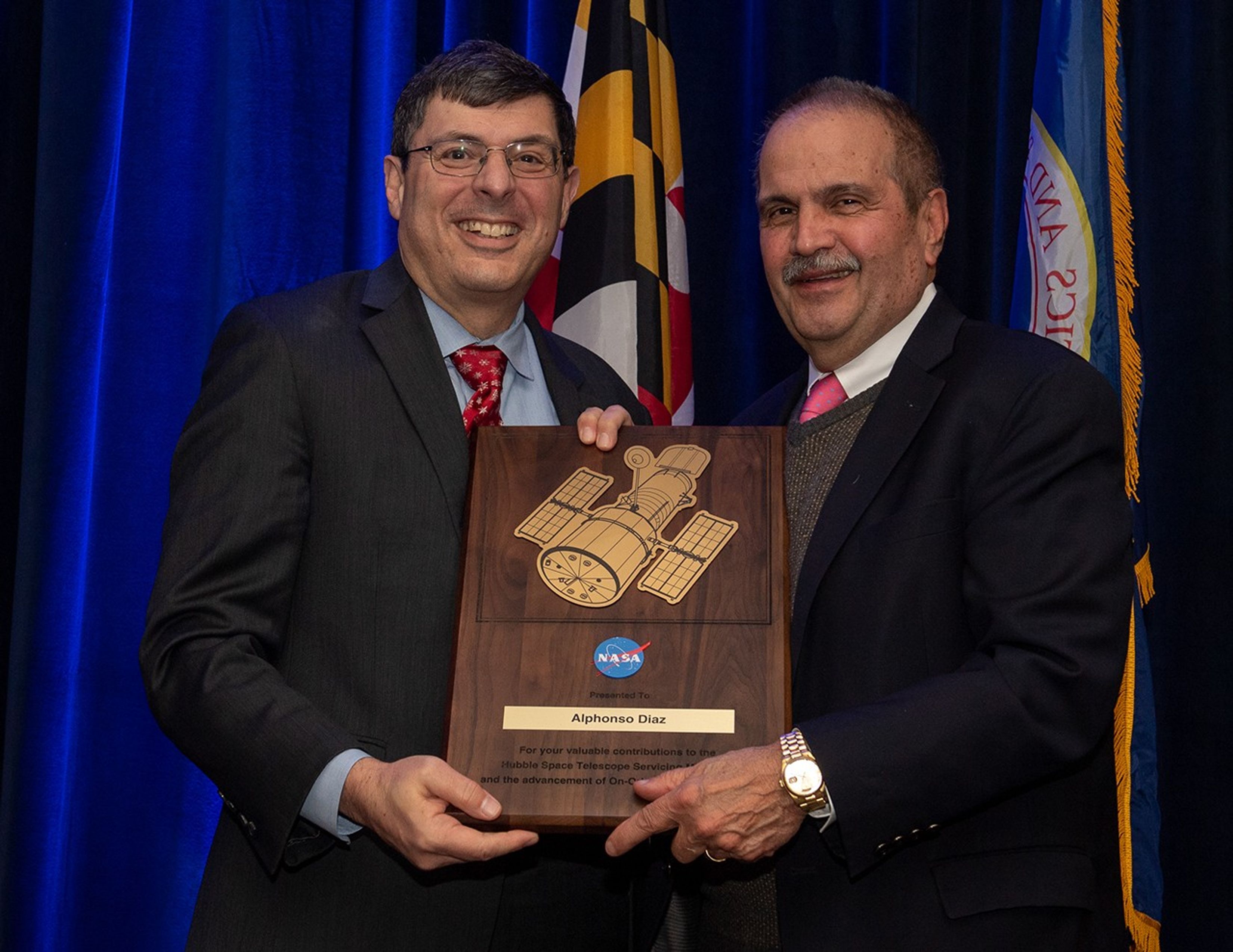 Scolese (left) and Diaz (right) hold a wooden plaque between them with Diaz's name and a gold graphic of Hubble on it.