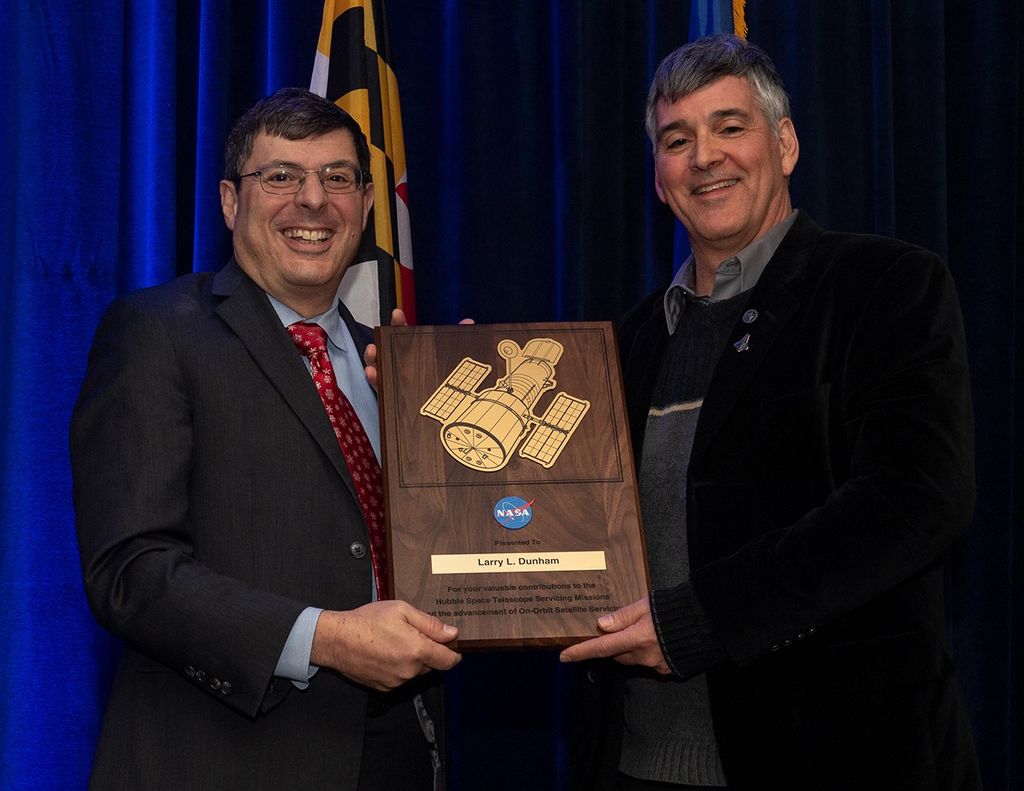 Scolese (left) and Dunham (right) hold a wooden plaque between them with Dunham's name and a gold graphic of Hubble on it.