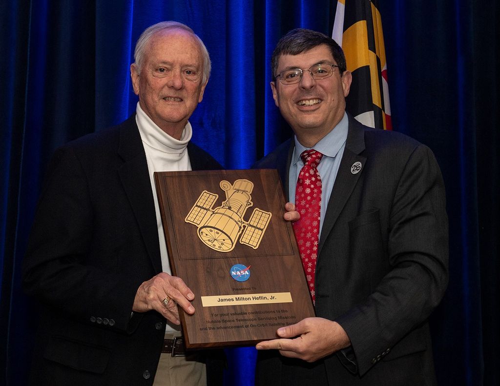 Scolese (right) and Heflin (left) hold a wooden plaque between them with Heflin's name and a gold graphic of Hubble on it.