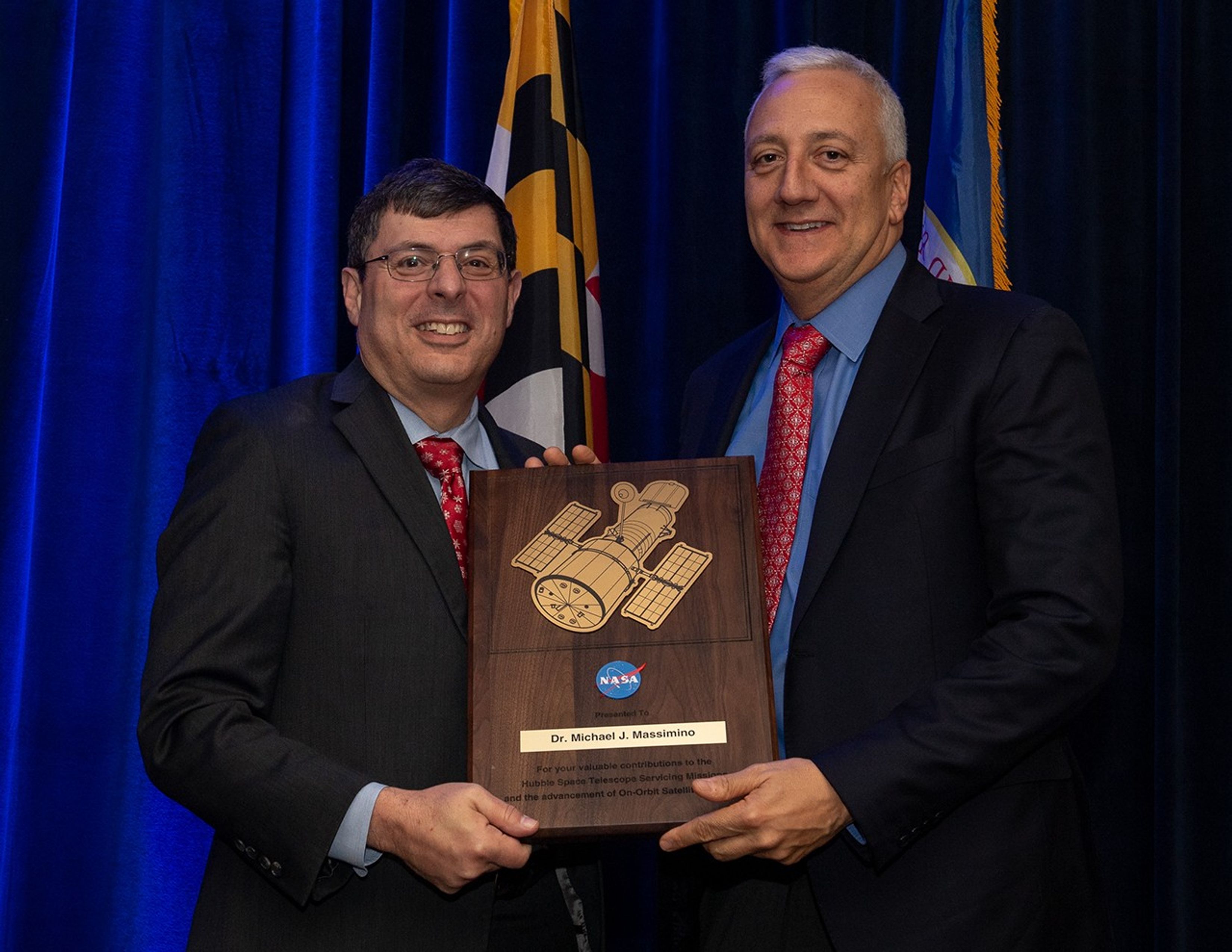Scolese (left) and Massimino (right) hold a wooden plaque between them with Massimino's name and a gold graphic of Hubble on it.