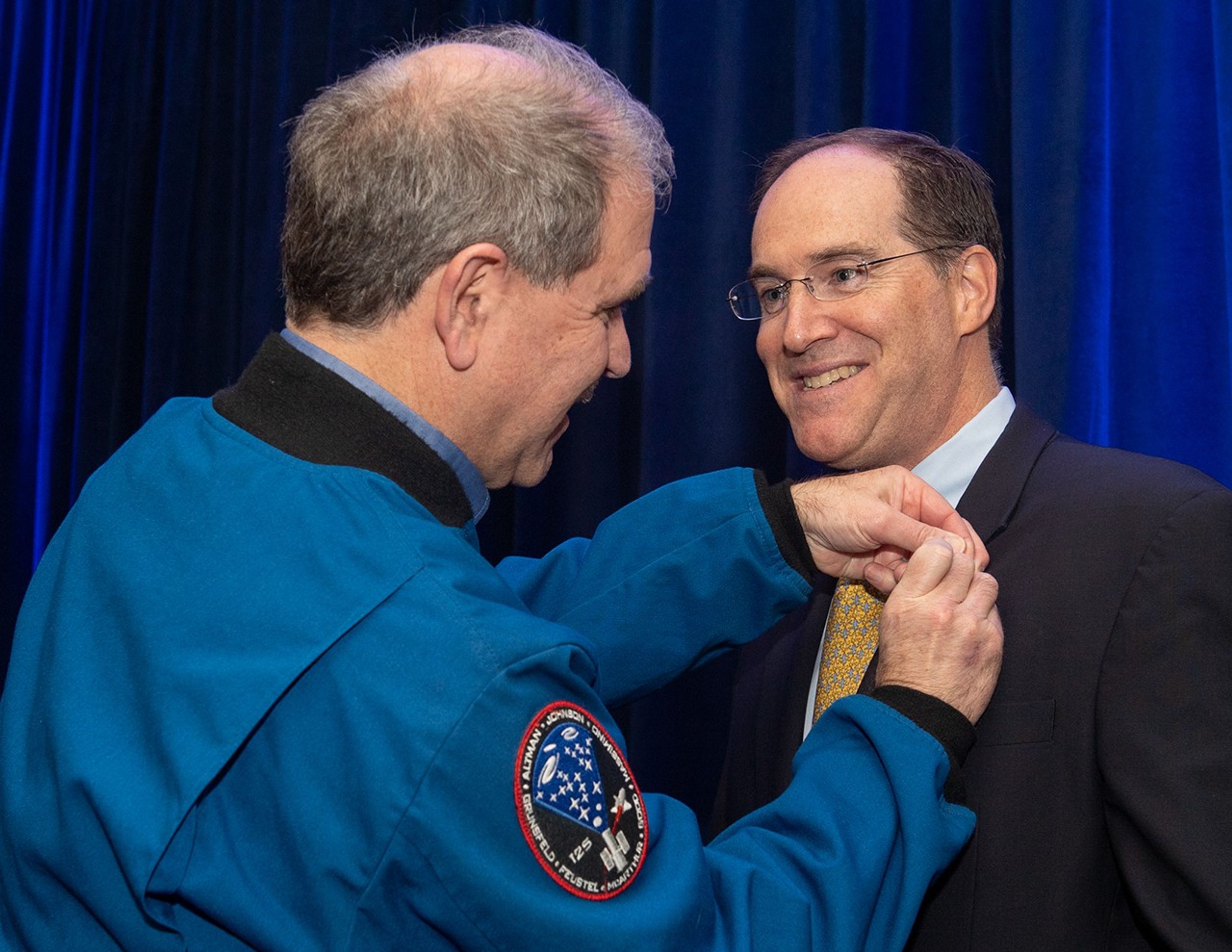 John Grunsfeld, left, puts a pin onto the lapel of the black suit of Justin Cassidy, right.