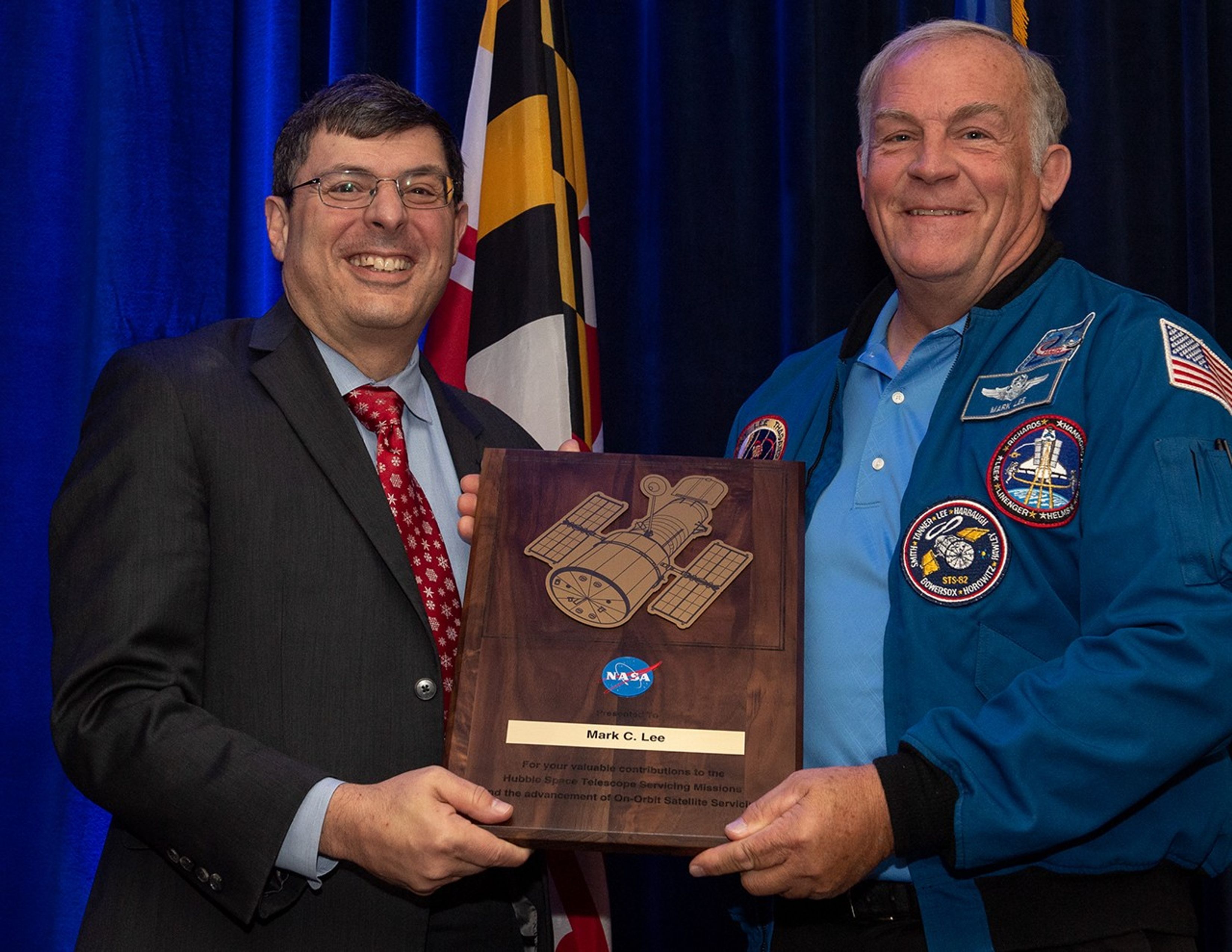 Scolese (left) and Lee (right) hold a wooden plaque between them with Lee's name and a gold graphic of Hubble on it.
