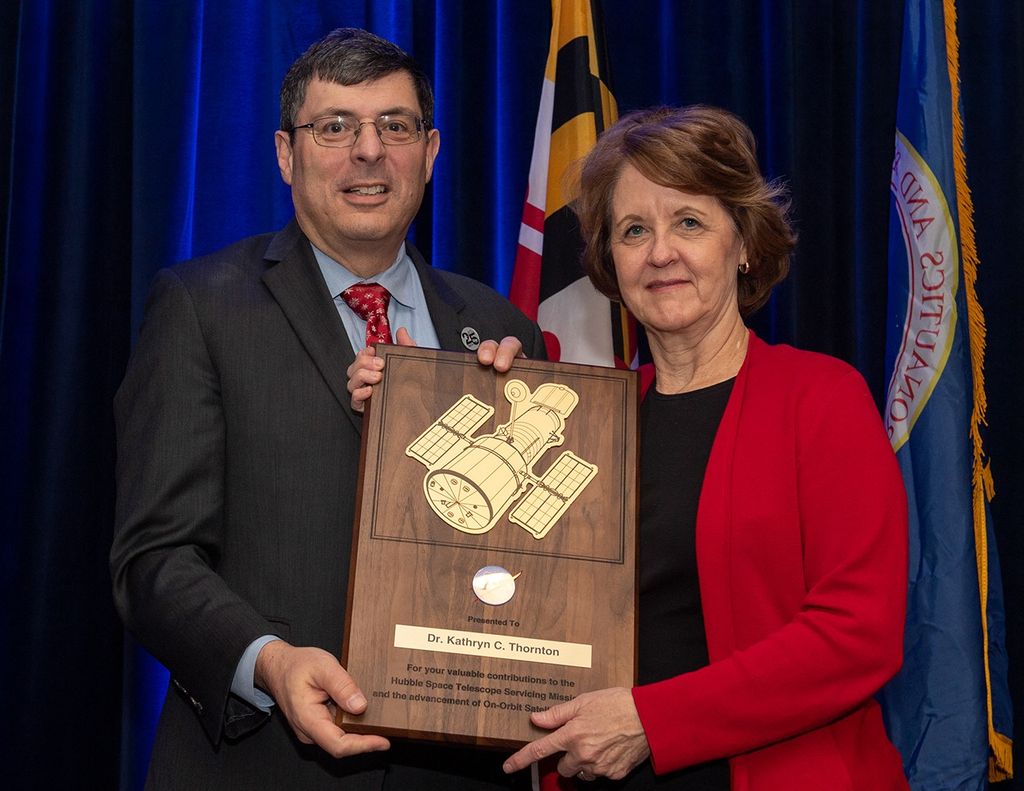 Scolese (left) and Thornton (right) hold a wooden plaque between them with Thornton's name and a gold graphic of Hubble on it.