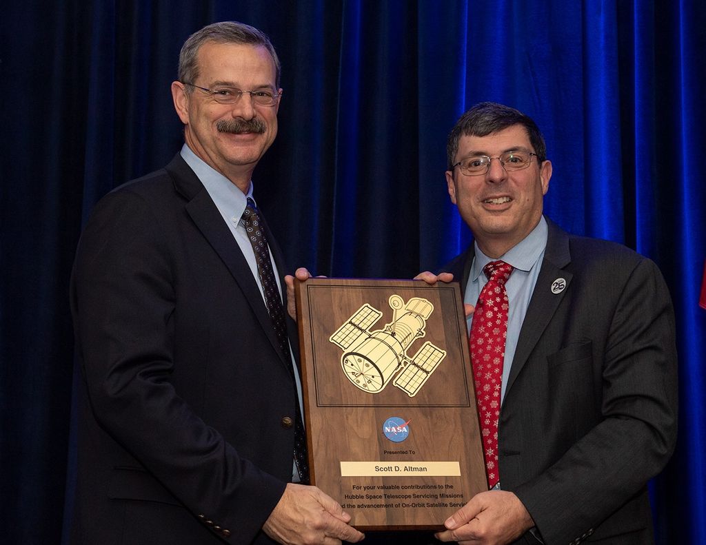 Scolese (right) and Altman (left) hold a wooden plaque between them with Altman's name and a gold graphic of Hubble on it.