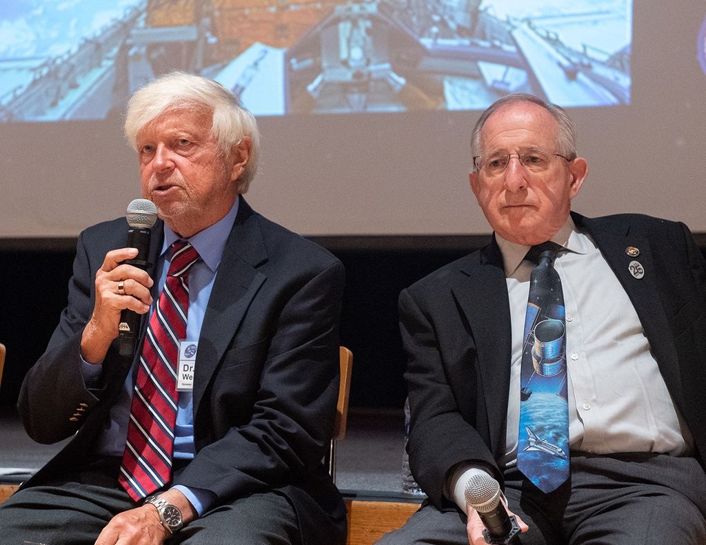 Ed Weiler, left, speaks into a microphone to address the audience, while Joseph Rothenberg, right, also holds a mic.