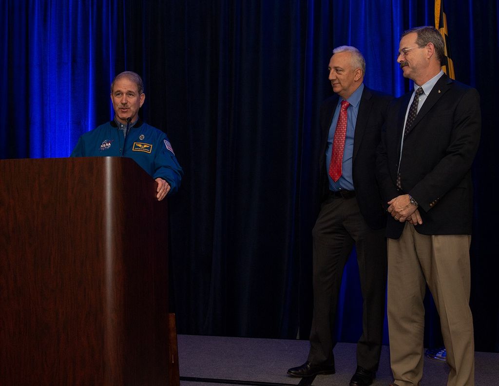 Grunsfeld (left) speaks at the podium while Massimino and Altman watch from the right.