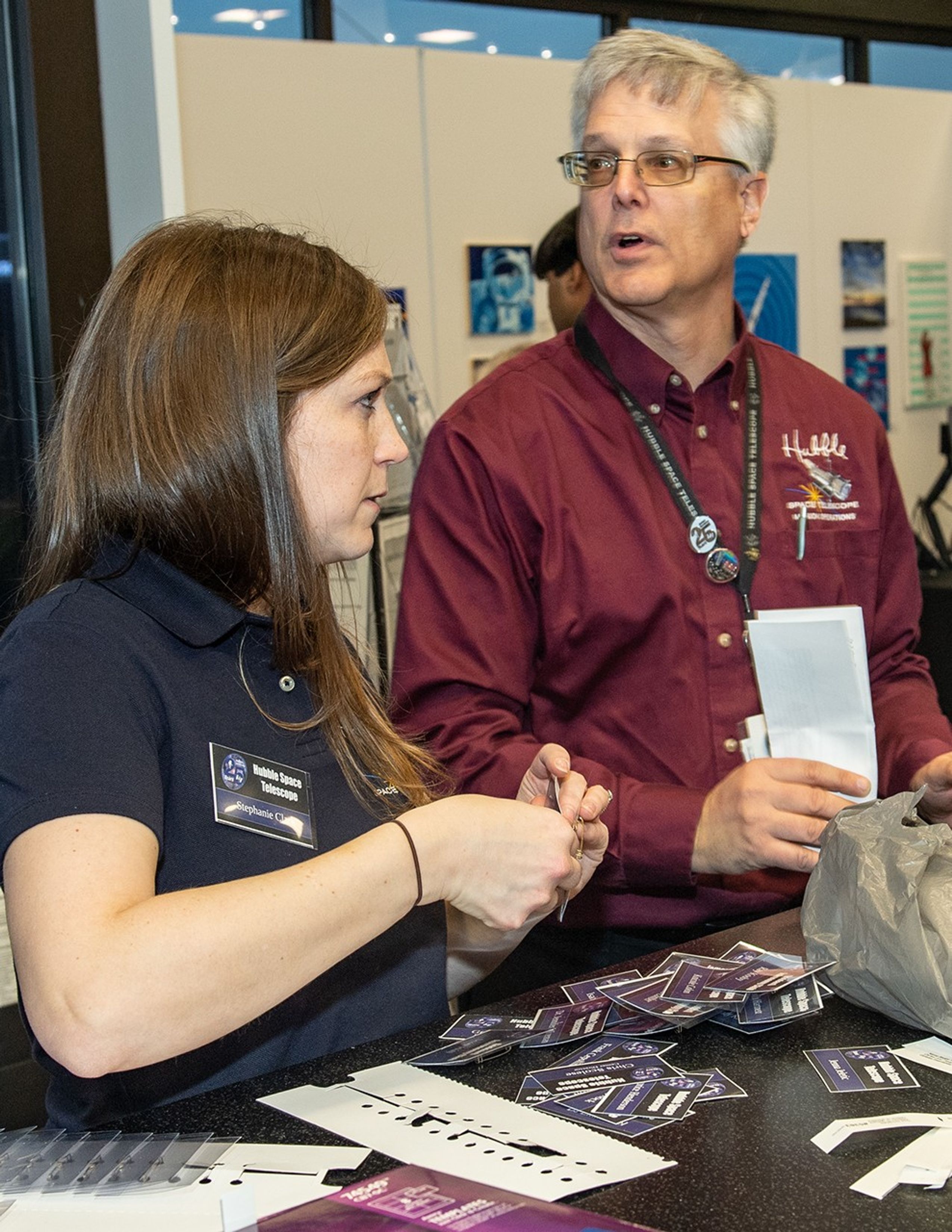 Stephanie Clark (left) and Jim Jeletic (right) put together name badges, with a visitor visible in the background.