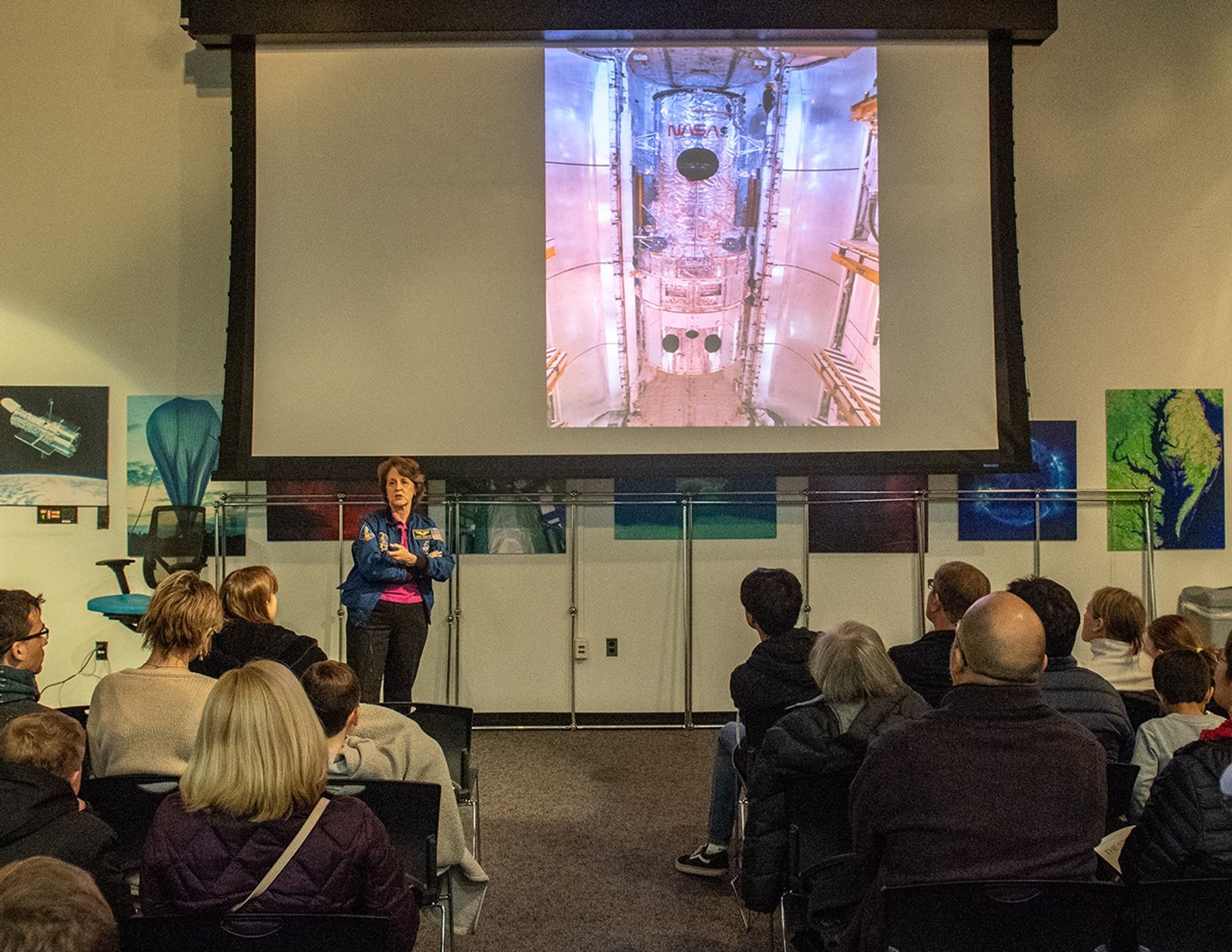 Kathy Thornton speaks to a listening audience, with a picture of Hubble on the slide on the screen above her.