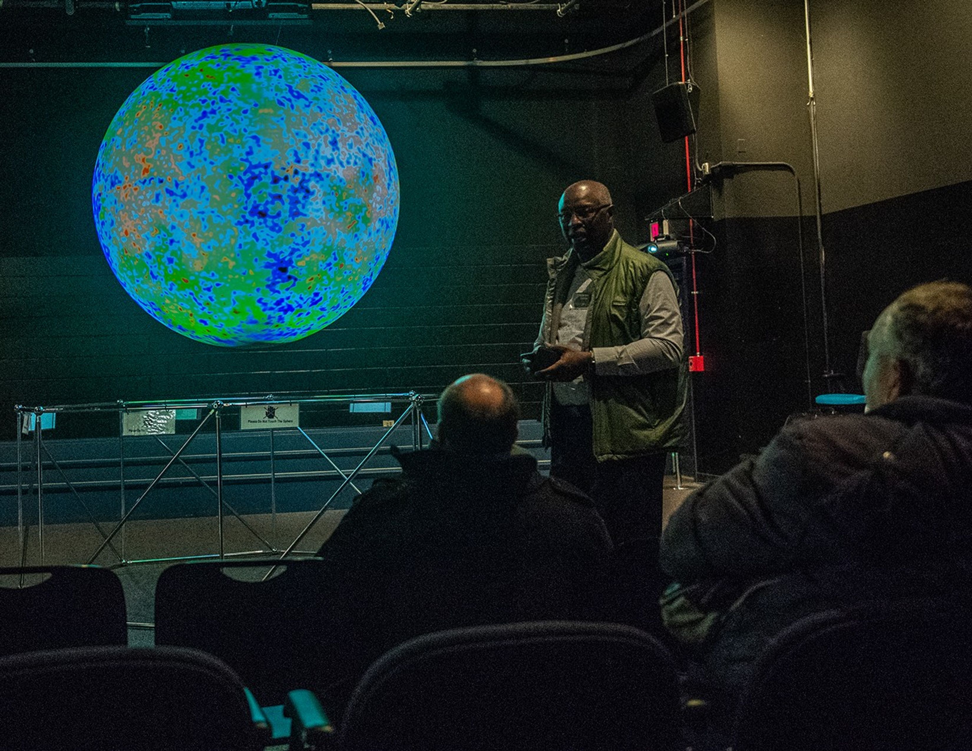 Maurice Henderson speaks to a listening audience, with a display projected onto a sphere behind him.