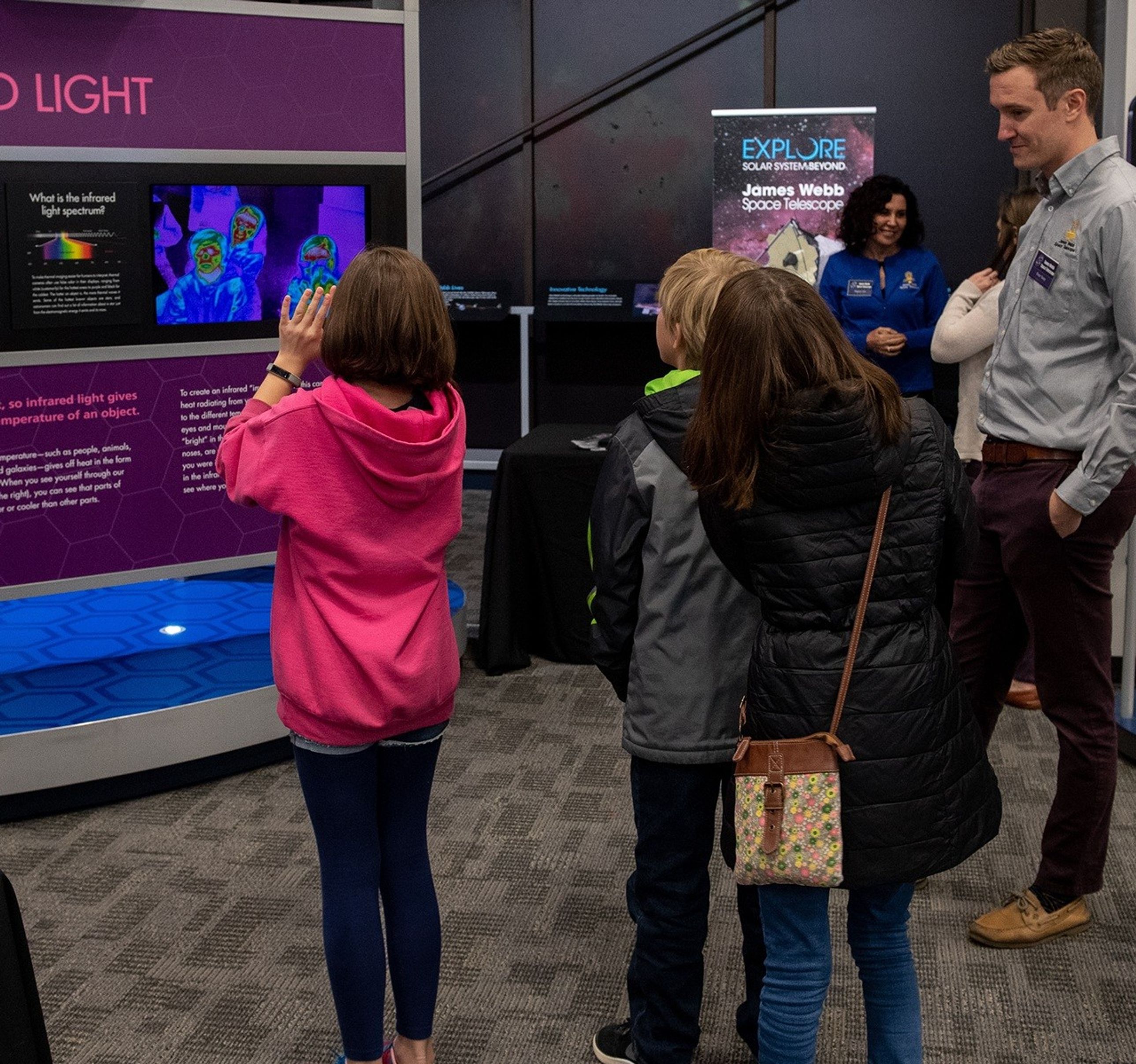 Sooy (right) watches as three young visitors (left) use the infrared camera display. Two more people converse in the background.