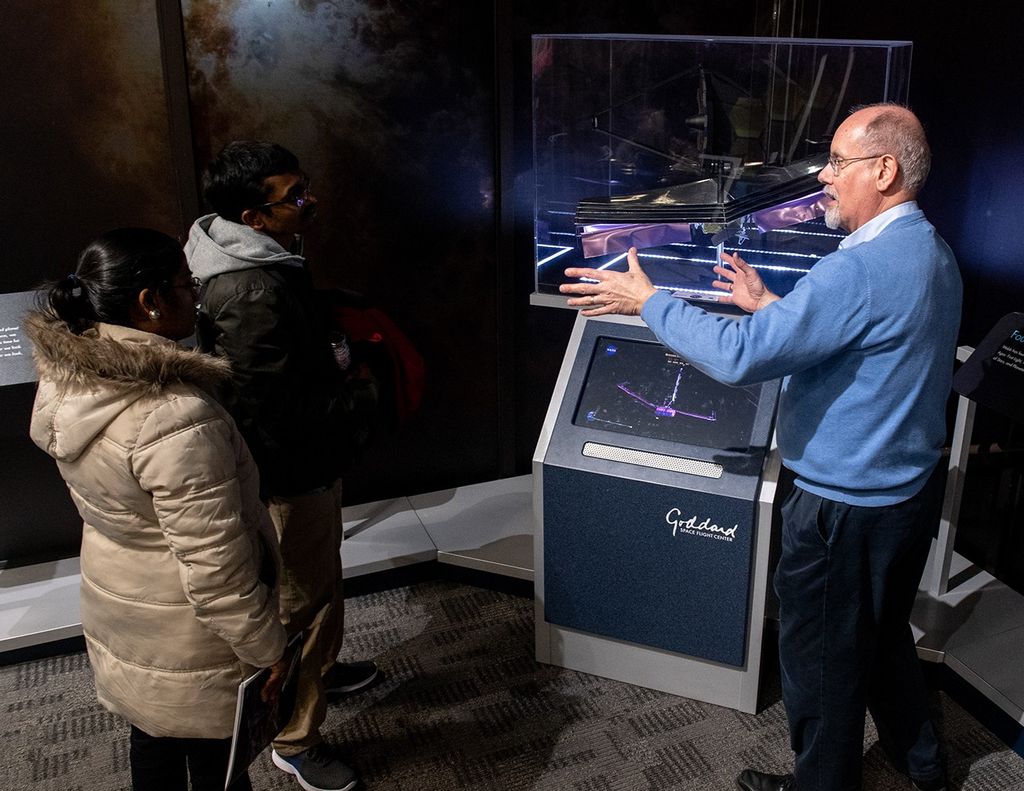 Randy Kimble, right, stands in front of a model of the Webb Space Telescope and talks about it to two visitors, left.