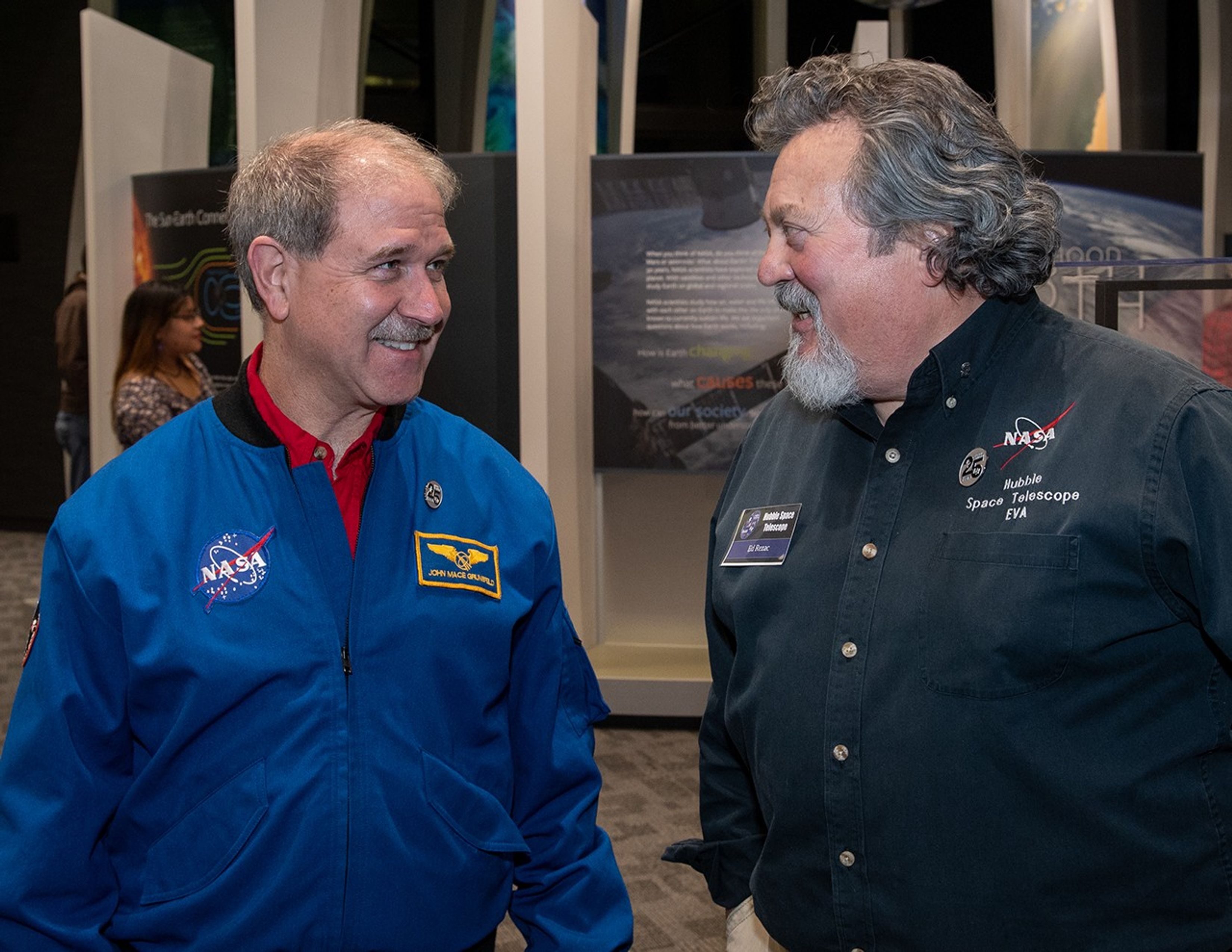 Grunsfelt (left) and Rezac (right) talk, with visitors visible in the background.