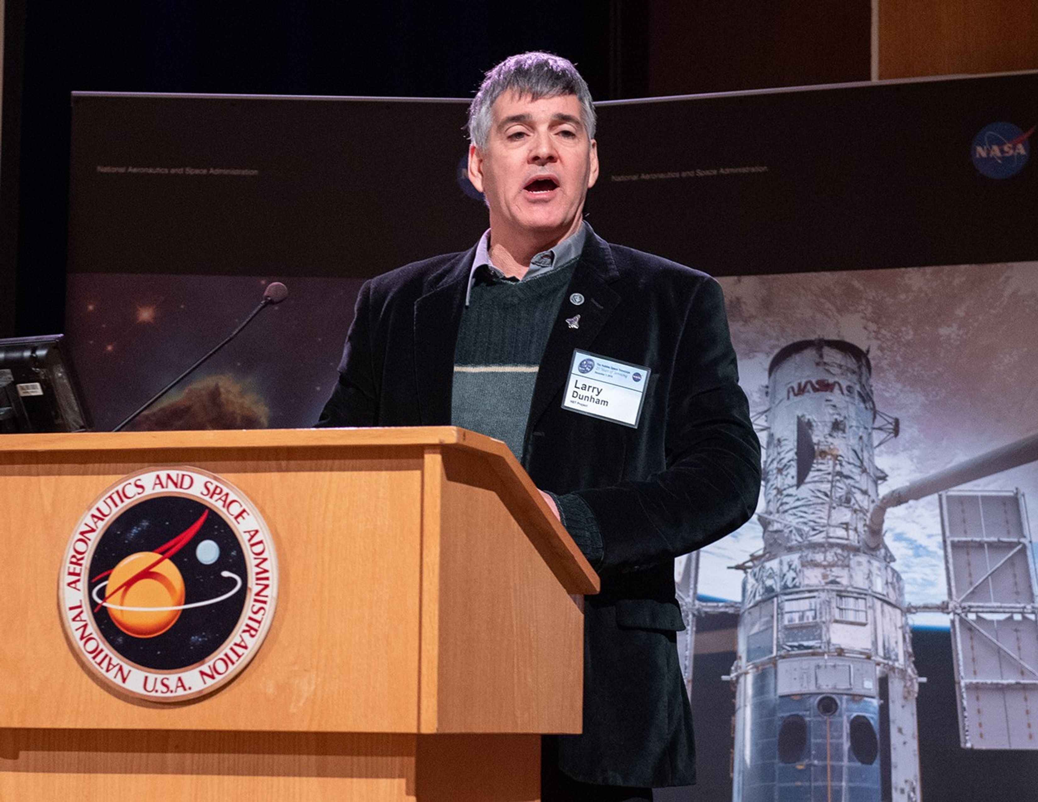 Larry Dunham stands at the NASA podium, addressing the audience.