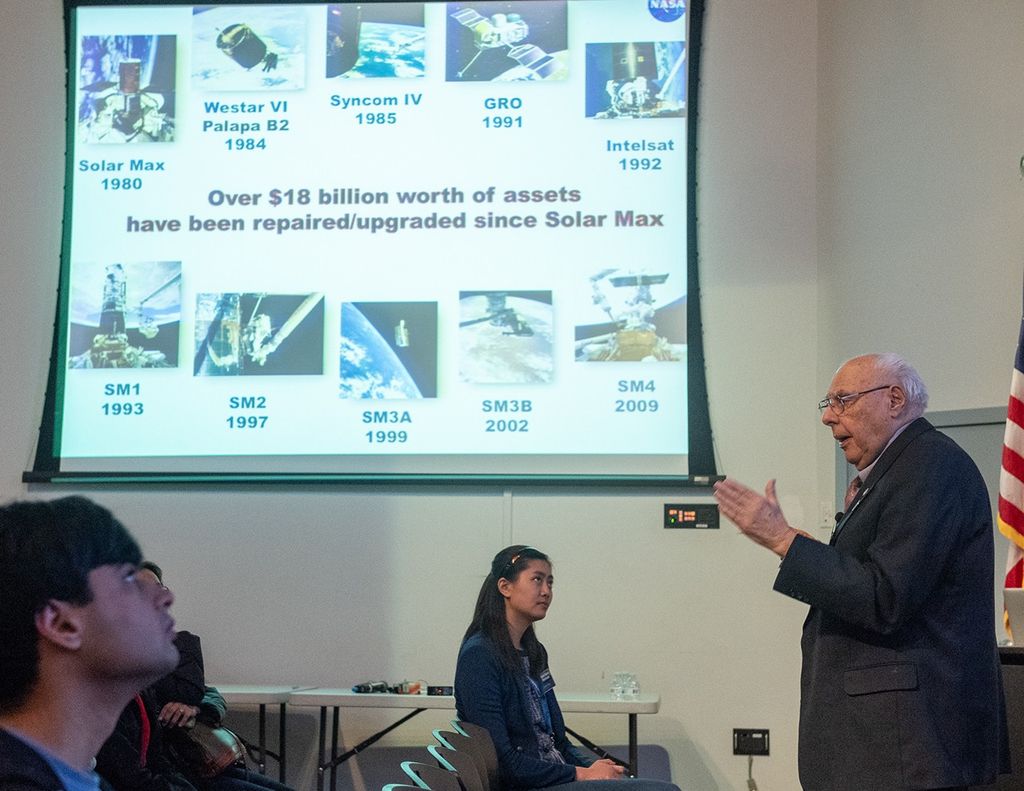 Frank Cepollina (right) speaks to a listening audience (left), with a slide show above them.