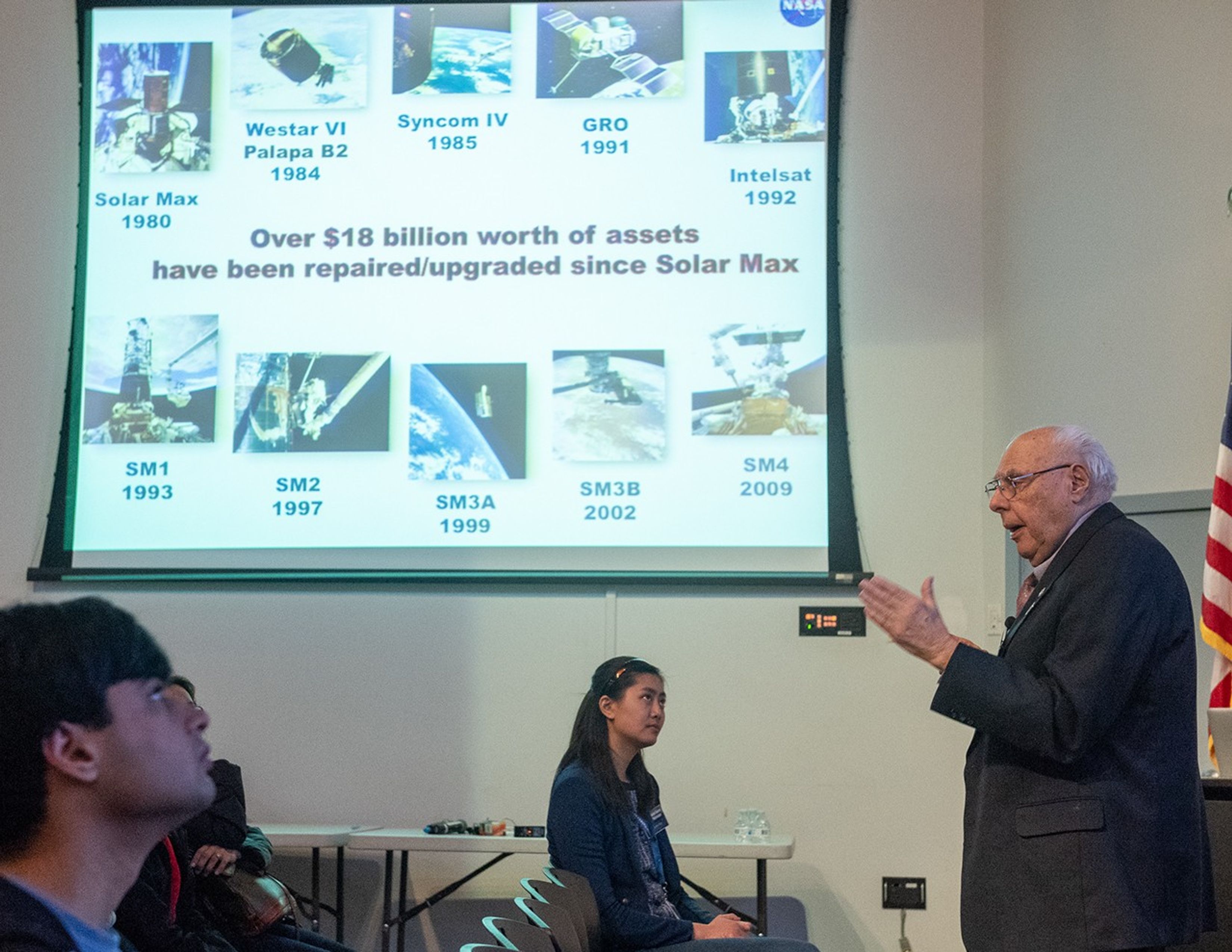Frank Cepollina (right) speaks to a listening audience (left), with a slide show above them.