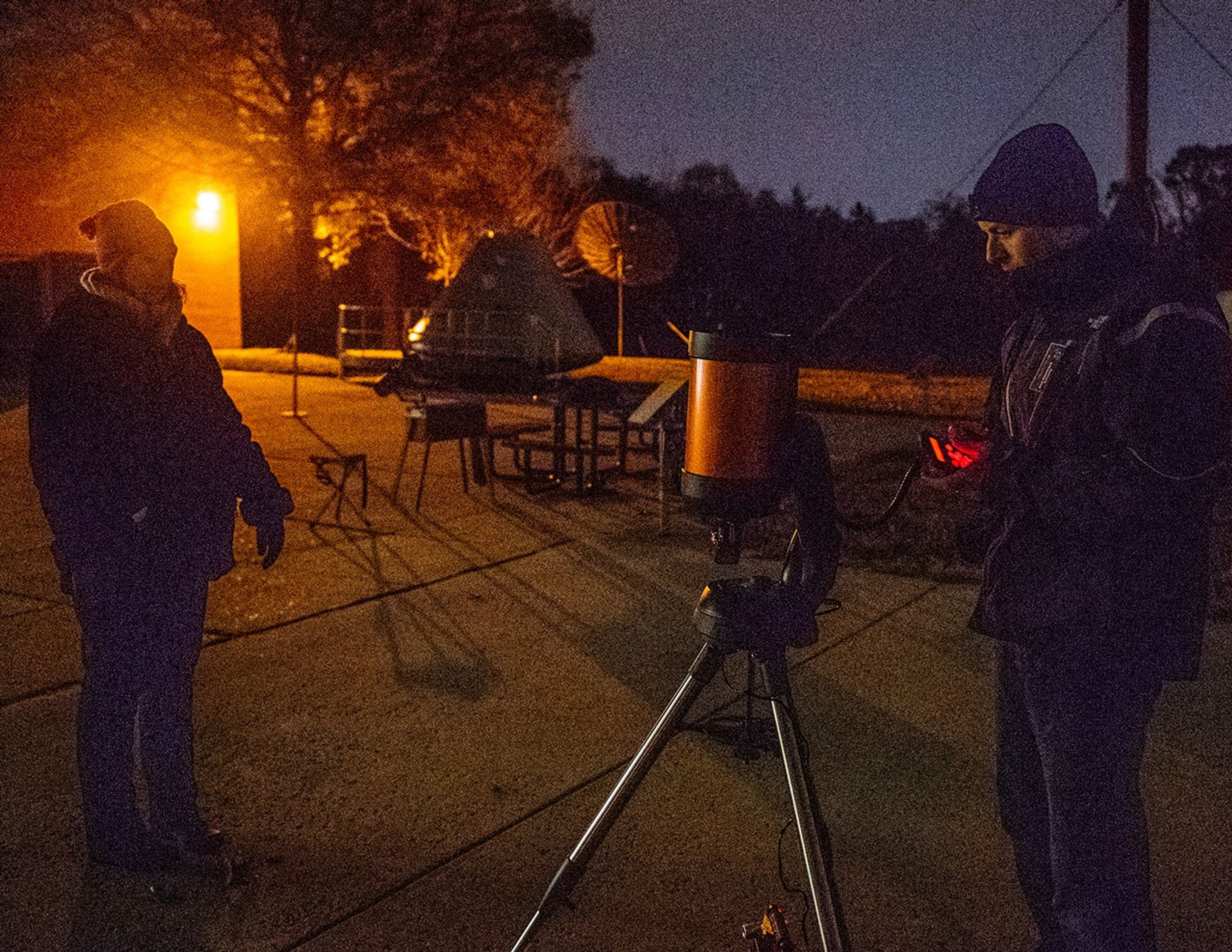 An astronomer (right) calibrates a telescope, while a guest (left) waits to use it.