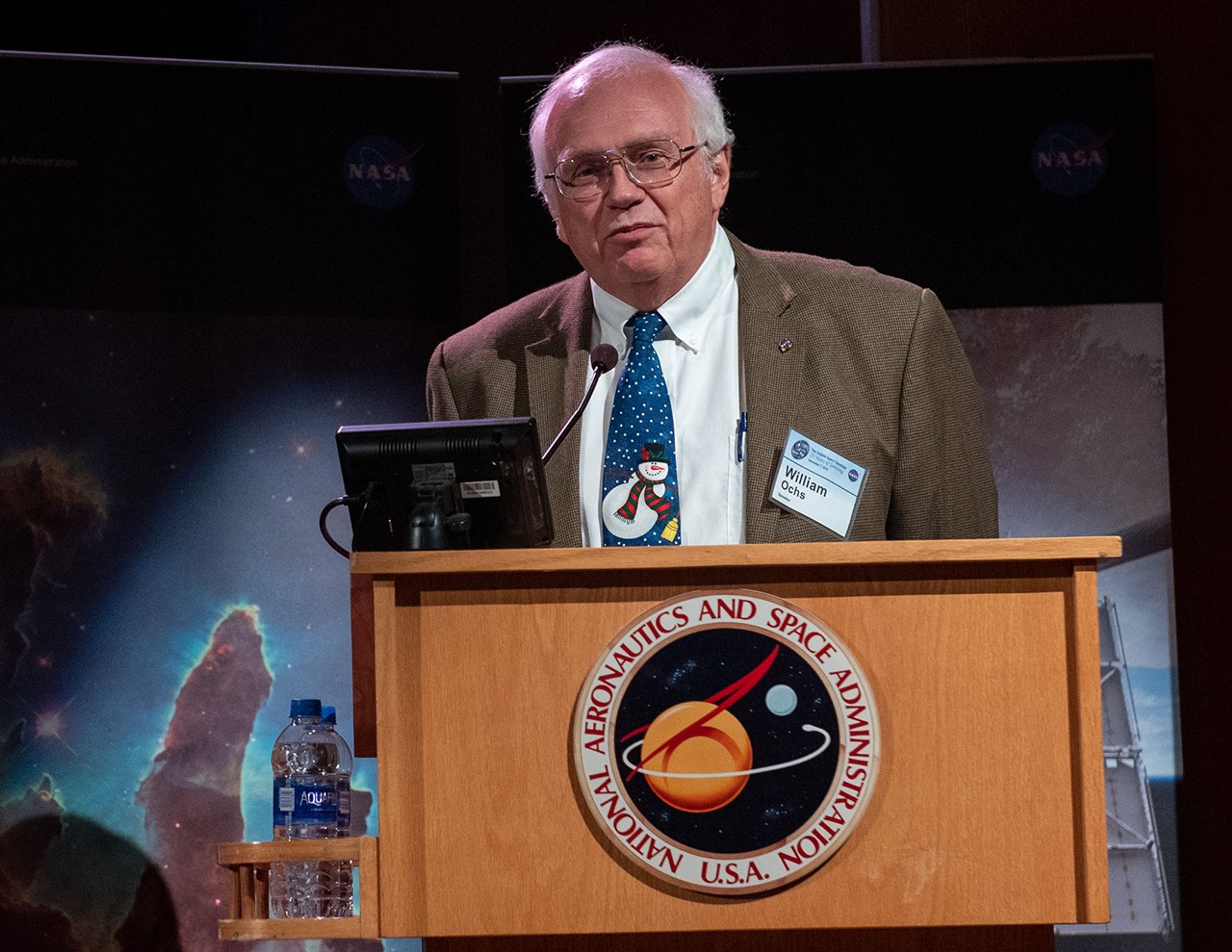 William Ochs stands at the NASA podium, addressing the audience.