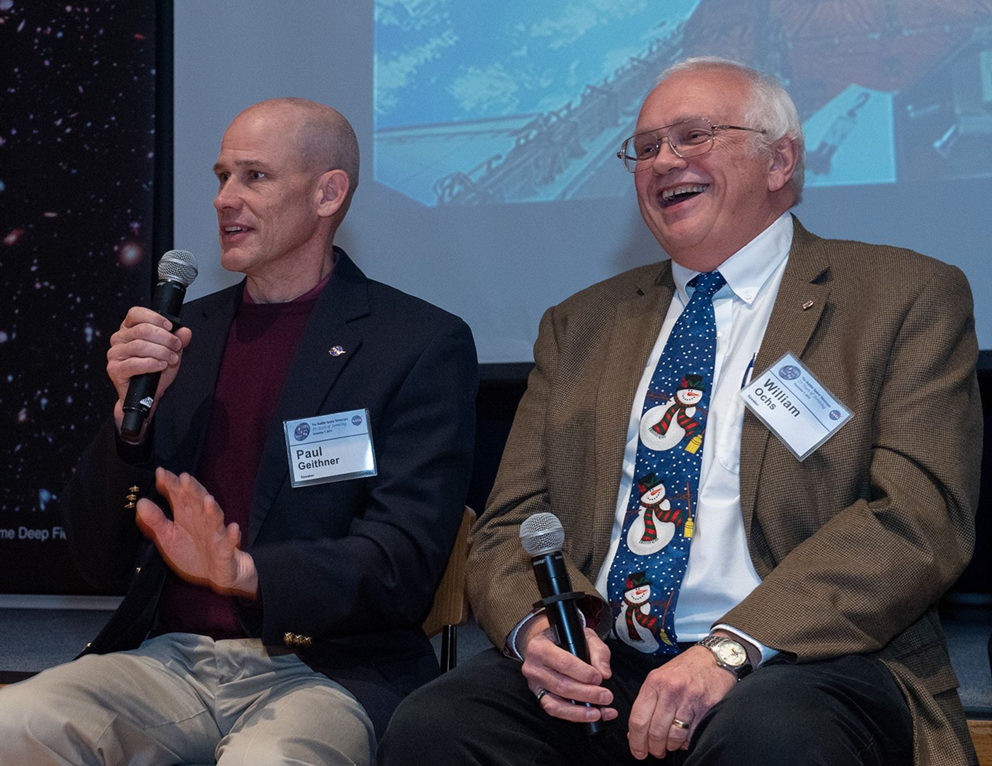 Paul Geithner, left, uses a microphone to address the audience, while William Ochs, right, laughs in reaction to his words and holds a mic of his own.