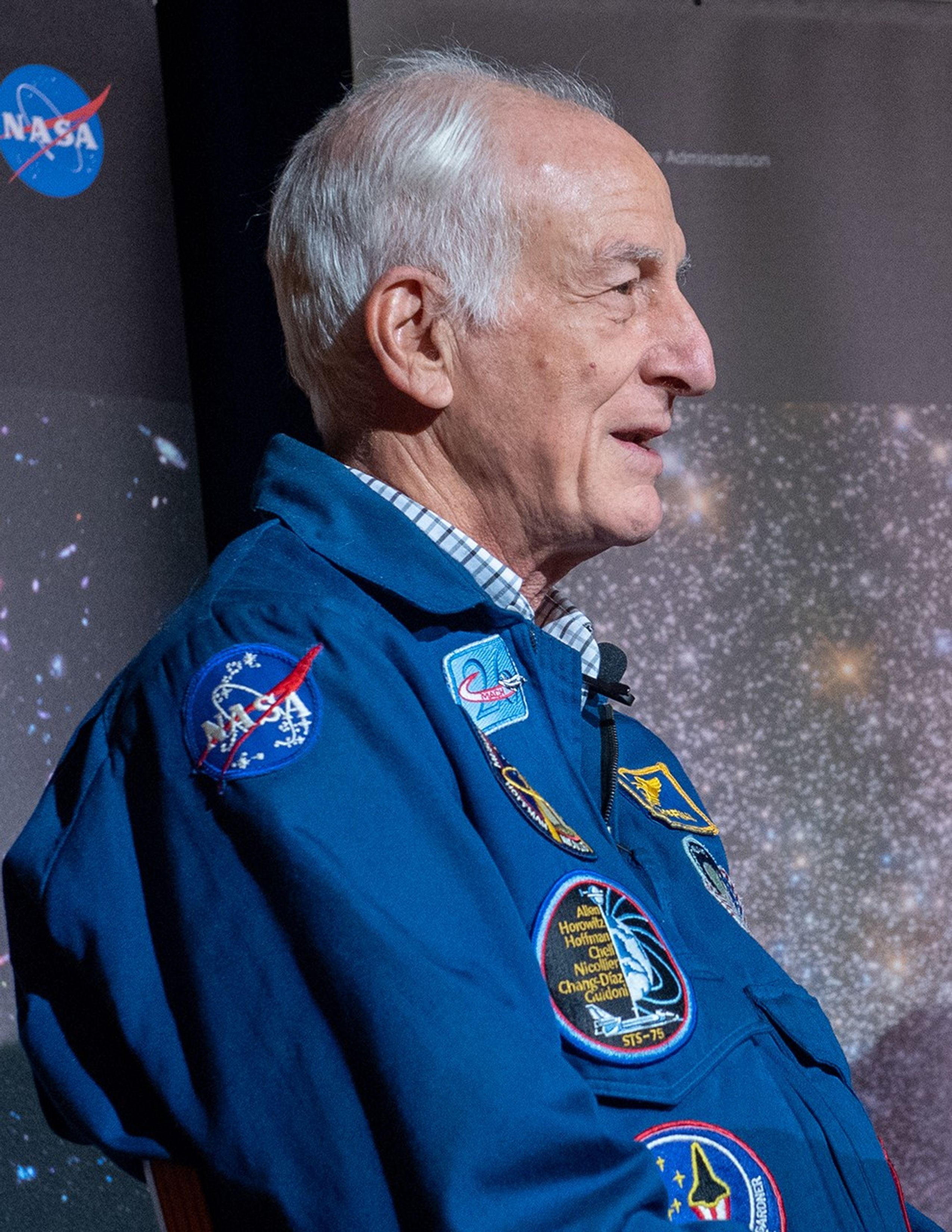 Astronaut Hoffman faces toward the right side of the image, speaking on a panel.