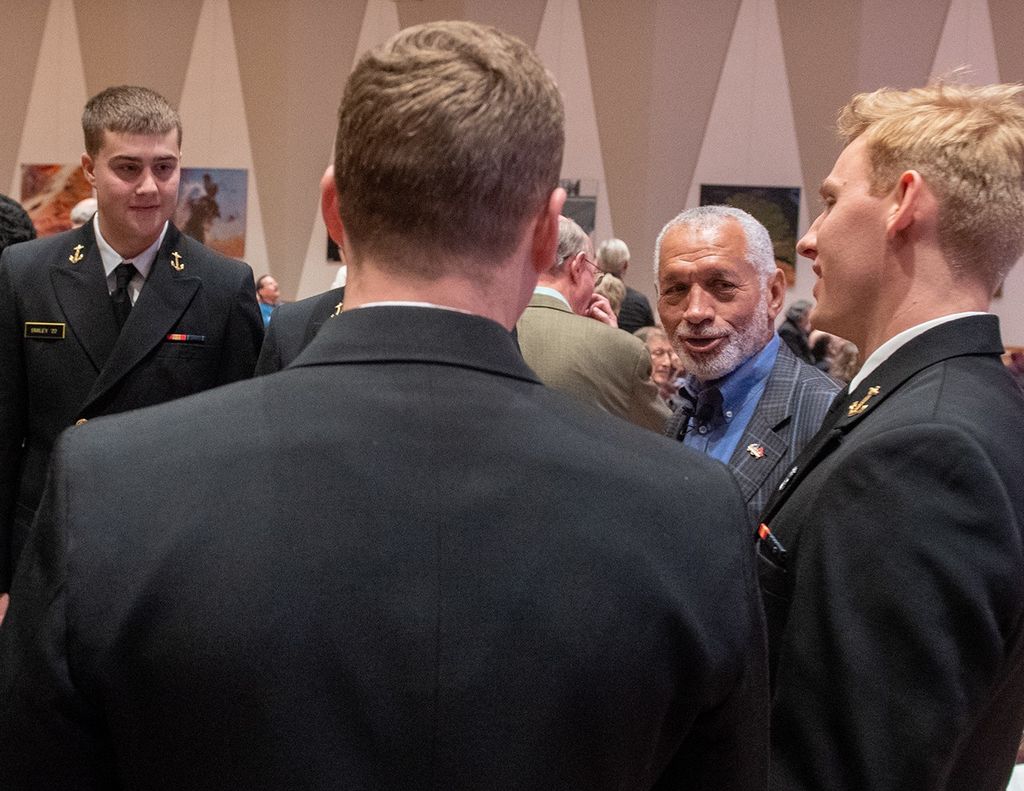 Charlie Bolden talks to four young Navy midshipmen; one faces towards the camera, one toward the left side of the image, one with his back to the camera, and the fourth blocked from view by the third.