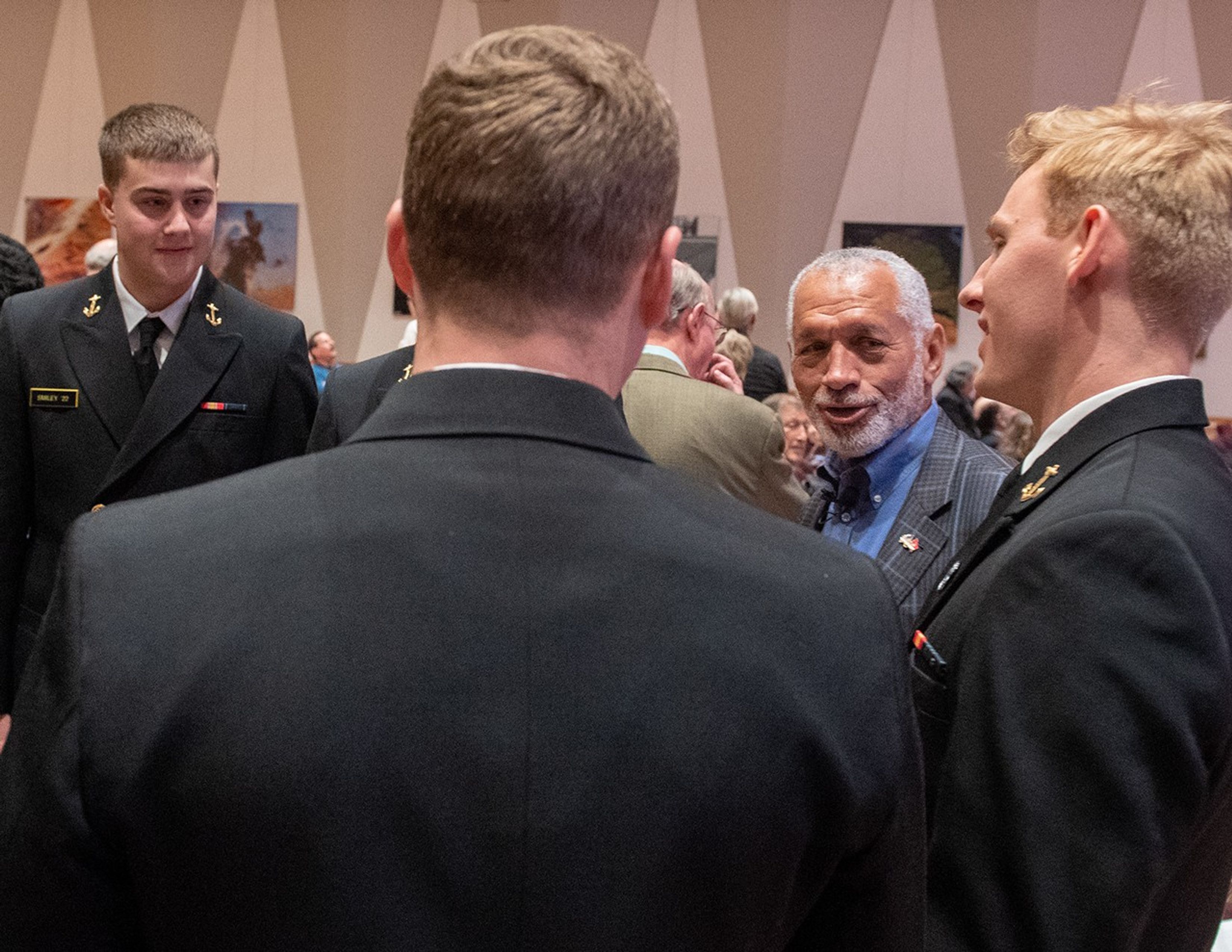 Charlie Bolden talks to four young Navy midshipmen; one faces towards the camera, one toward the left side of the image, one with his back to the camera, and the fourth blocked from view by the third.