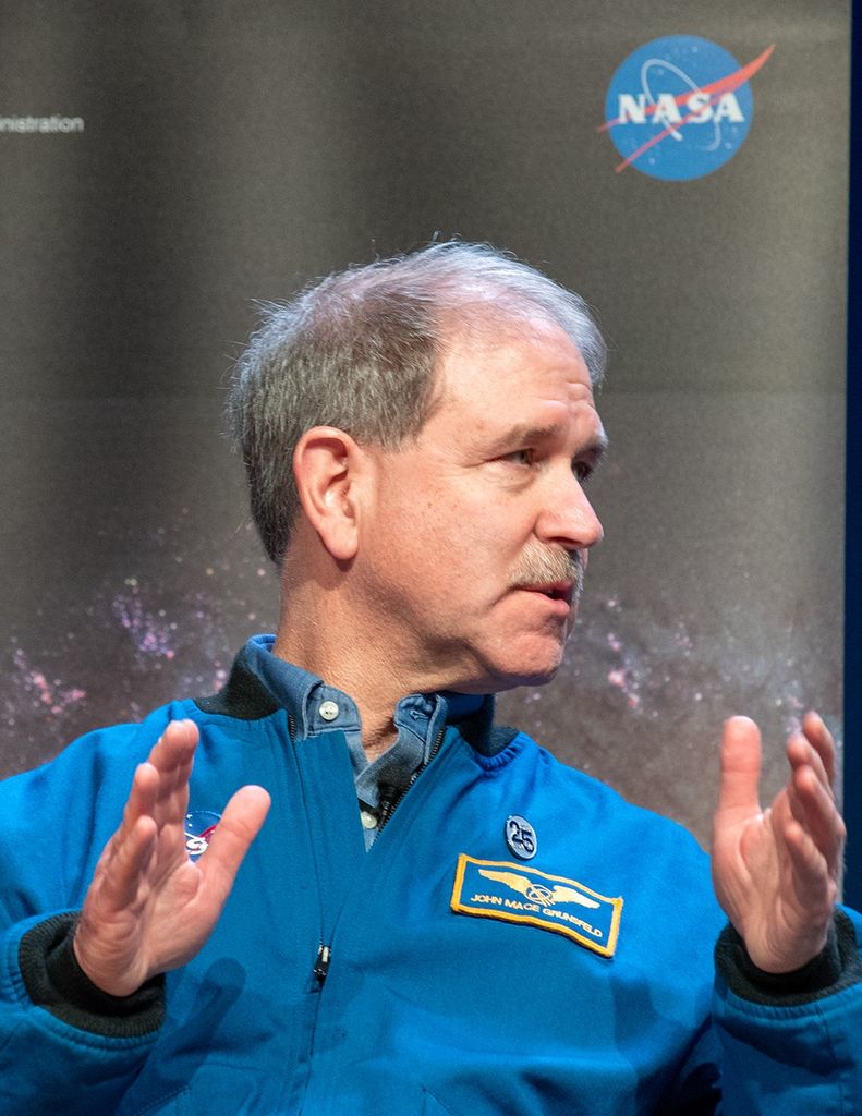 John Grunsfeld speaks to the audience while looking toward the right side of the image.