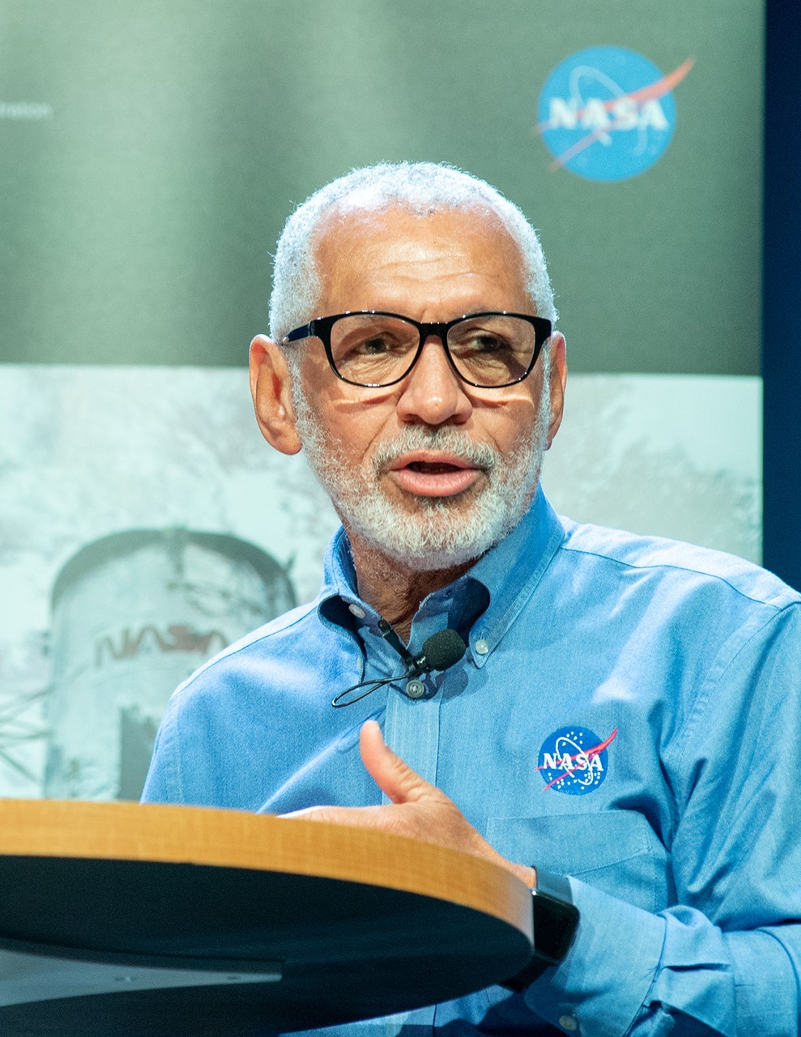 Charlie Bolden addresses the audience from a table onstage.