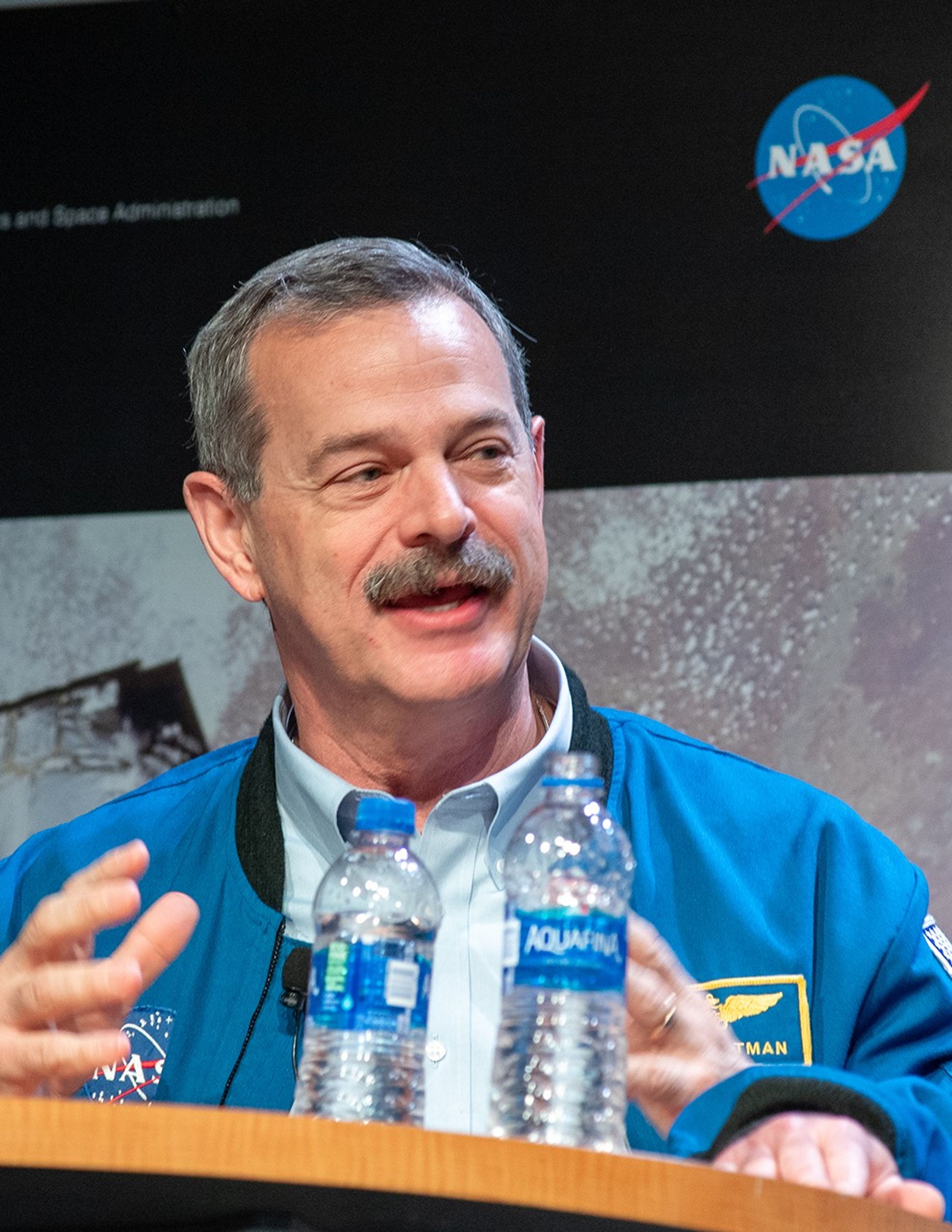Scott Altman sits at a table, speaking to the audience, with two water bottles in the foreground.